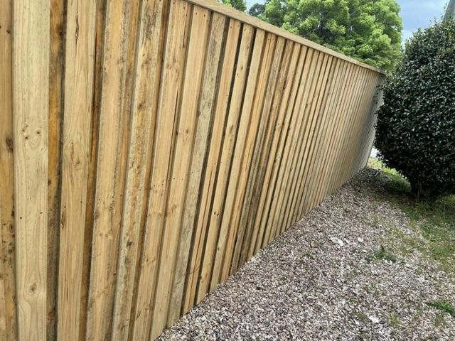 Wooden fence with vertical planks, gravel base, and green foliage nearby.