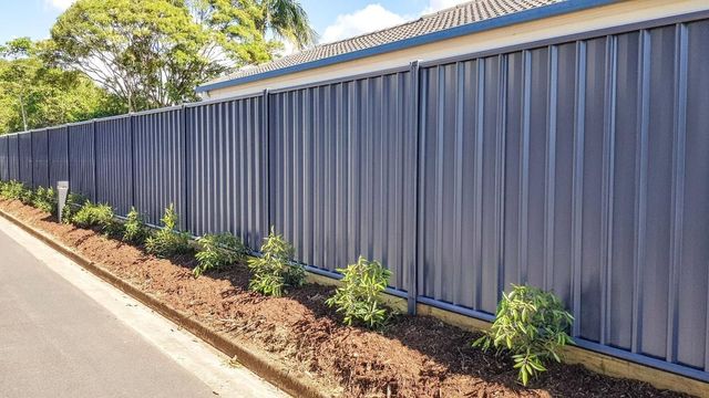A Blue Fence Is Sitting Next to A Rad Next to A House — Byron & Beyond Fencing In Billinudgel, NSW
