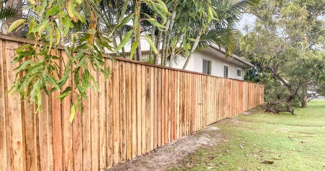 A Wooden Fence Is Surrounded by Grass and Trees in Front of A House — Byron & Beyond Fencing In Billinudgel, NSW