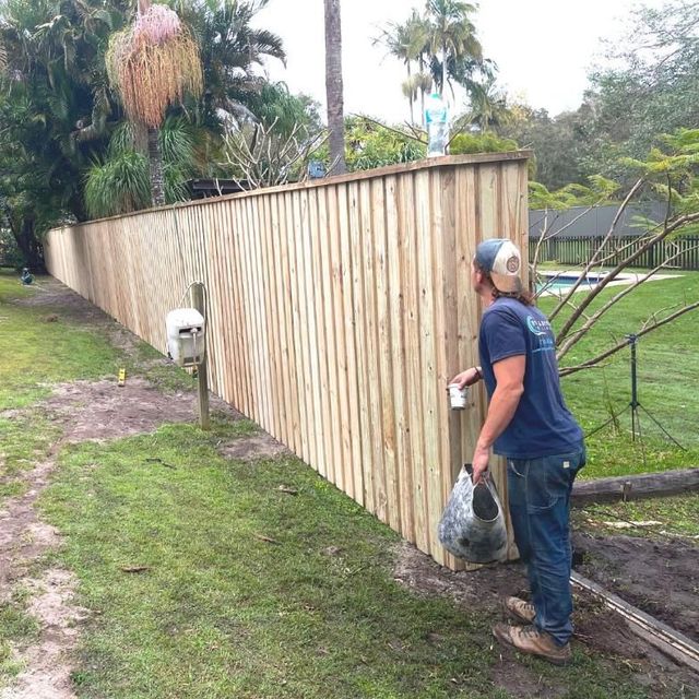 Person holding bag near new wooden fence and mailbox on grassy lawn.