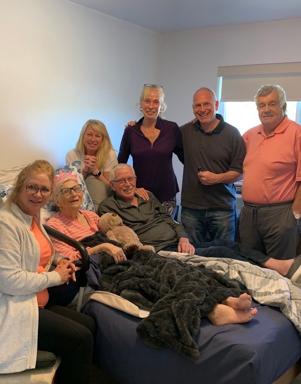 A group of people are posing for a picture with a man laying on a bed
