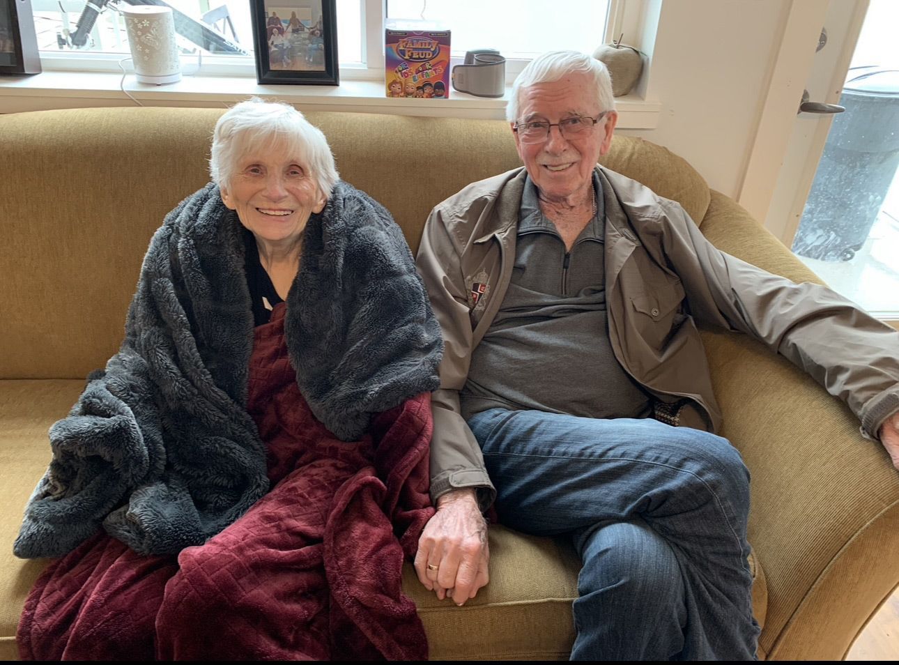 A man and a woman are sitting on a couch wrapped in blankets