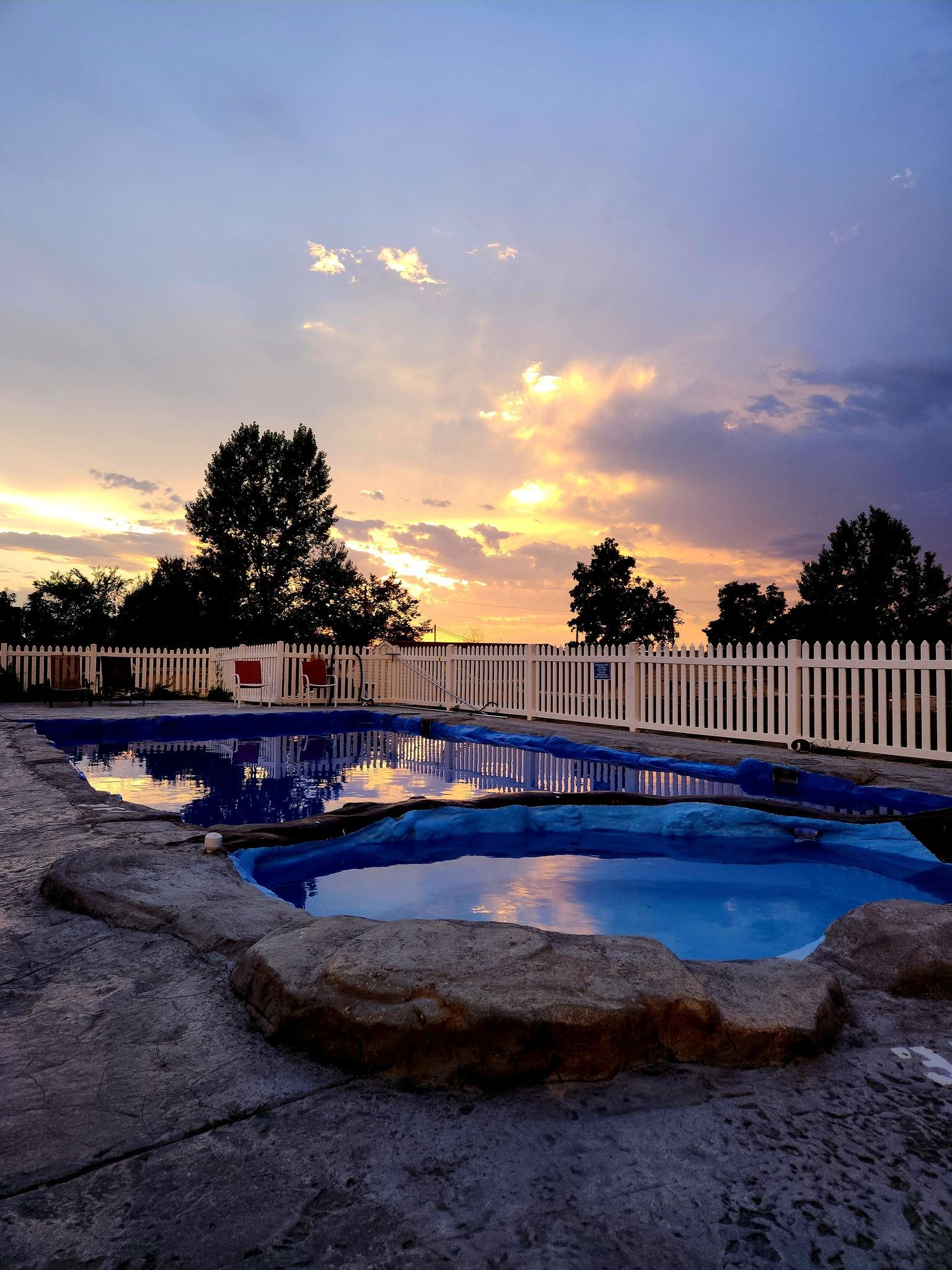 a pool with a white picket fence and a sunset in the background