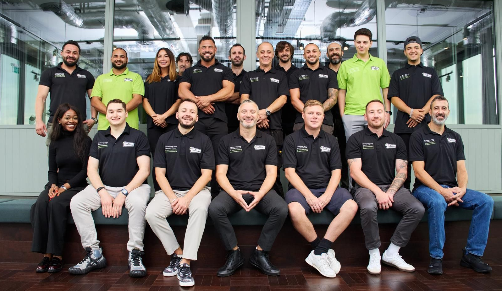 Group of people in black shirts posing in a modern office, some smiling.
