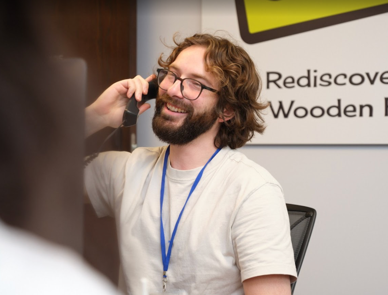 Person on phone, looking at laptop. White shirt, bun, blue nail polish, and gold ring.