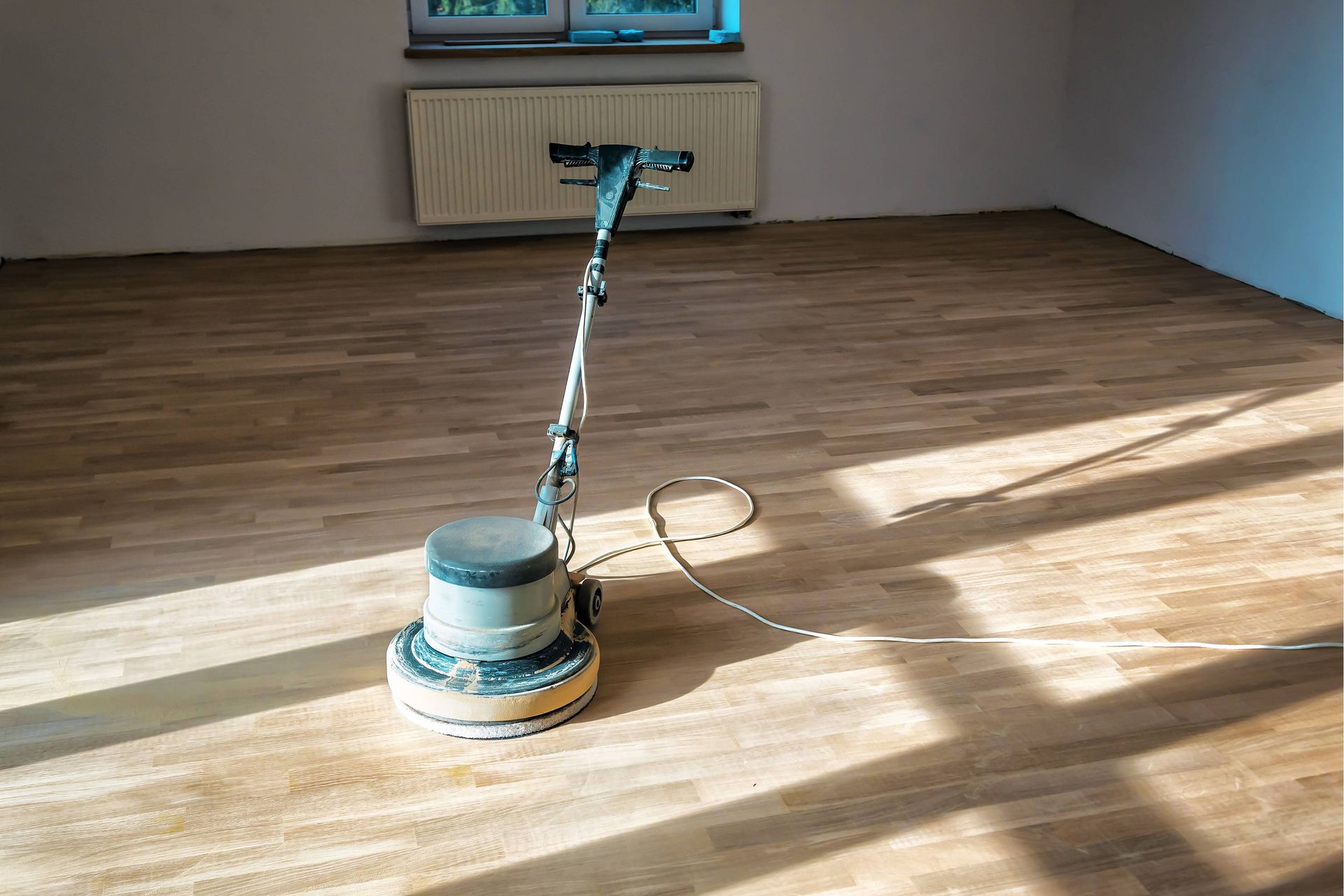 Floor sander on a wood floor in a room with a radiator and window.