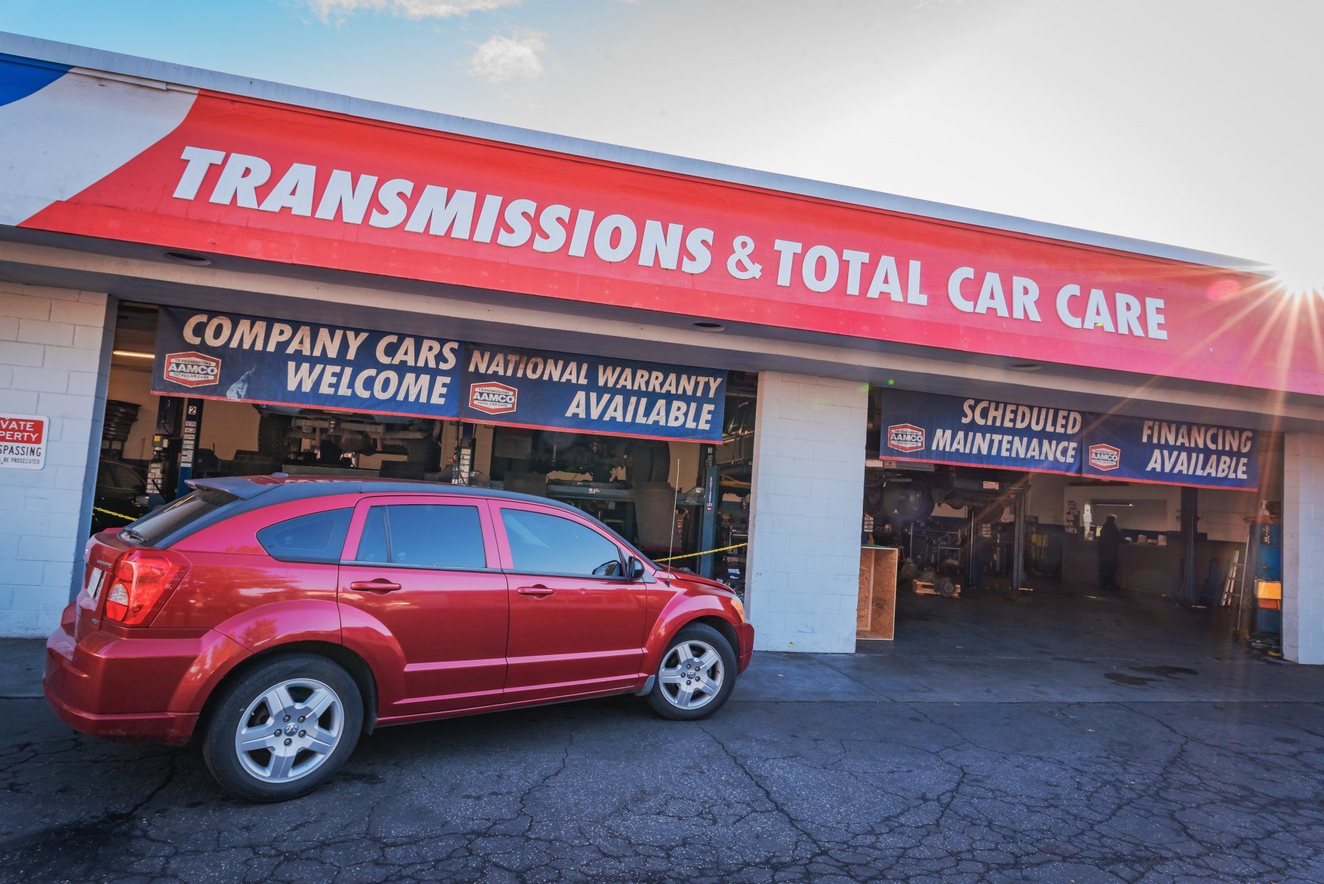 A red car is parked in front of a transmissions and total car care shop.