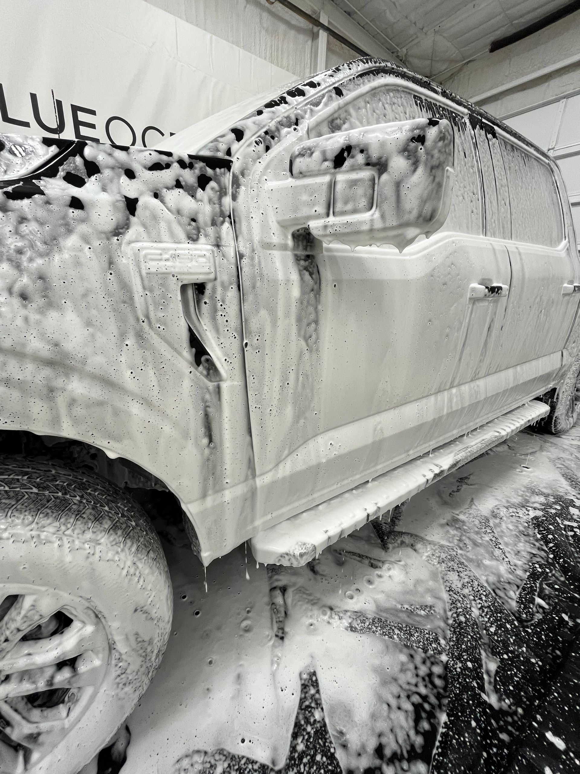 Hands smoothing out paint protection film on the front bumper of a blue truck near the headlight.
