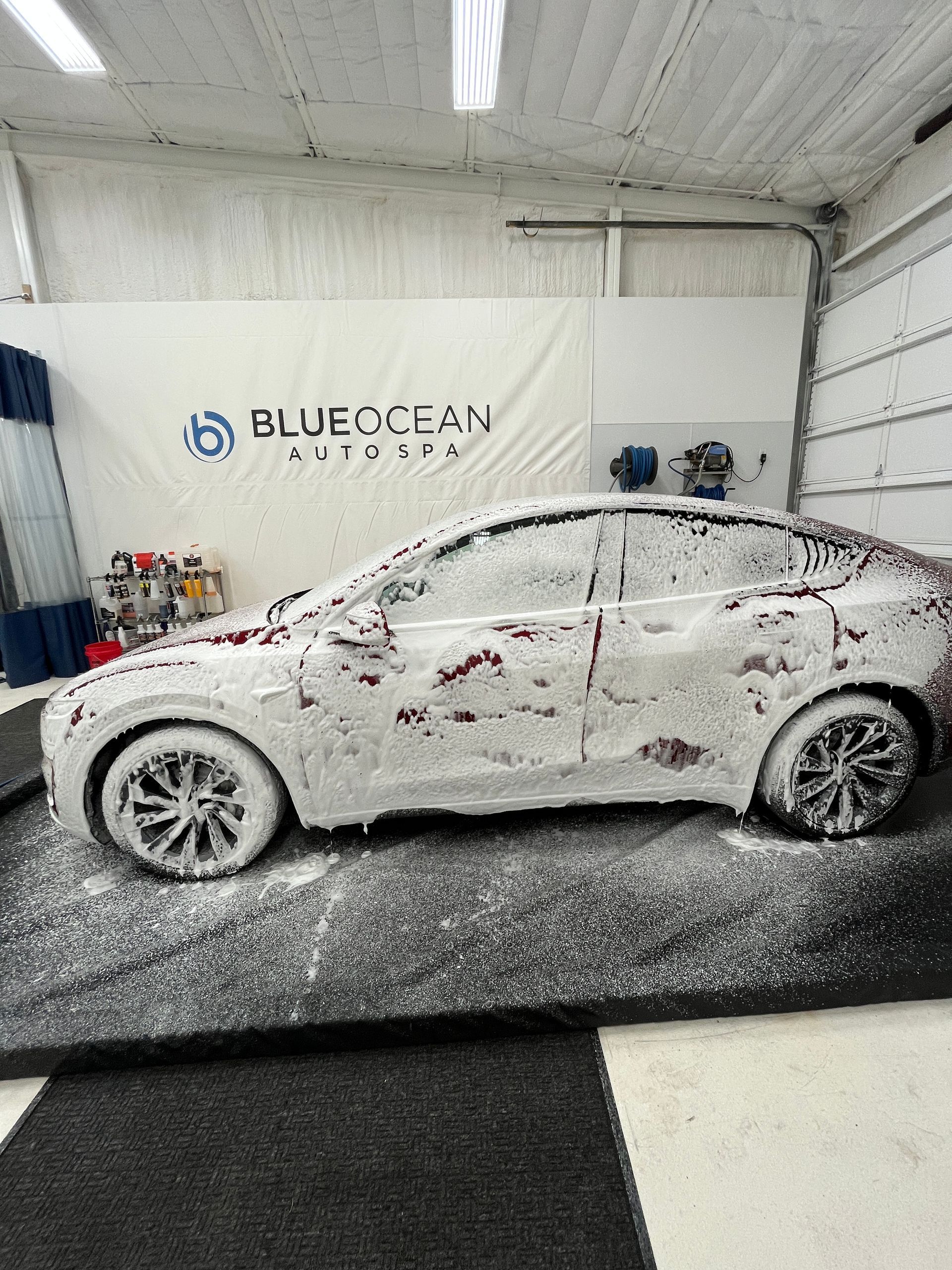 A 2026 Tesla Model Y exterior paint  and wheels are being sprayed down with a gentle snow foam to loosen bugs and road grime on the car.