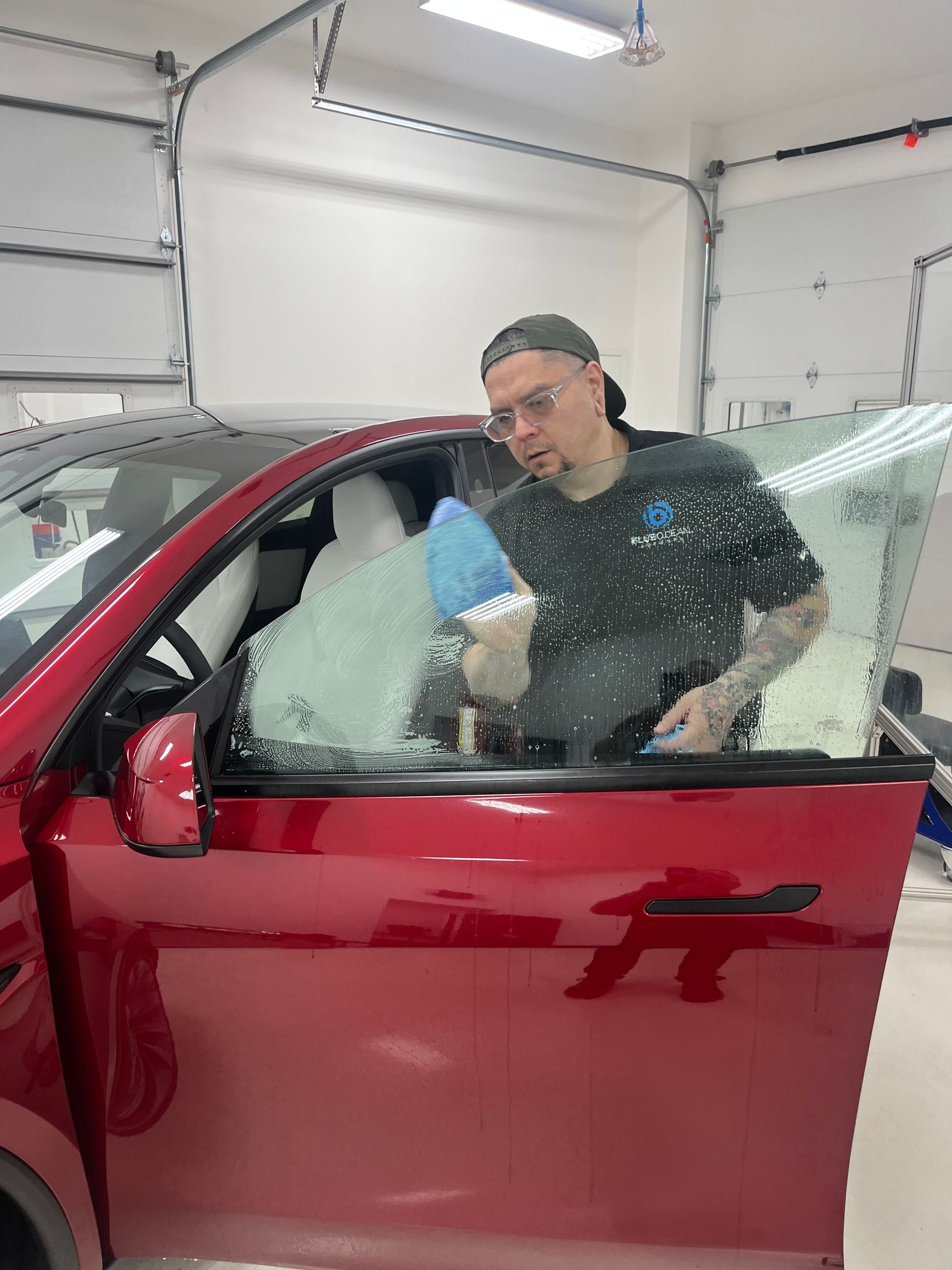 A window tint technician is preparing the front door window on this 2026 Tesla Model Y by cleaning the glass with    soap and a scratch free scrub pad in a clean room inside of Blue Ocean Auto Spa of Cedar Park