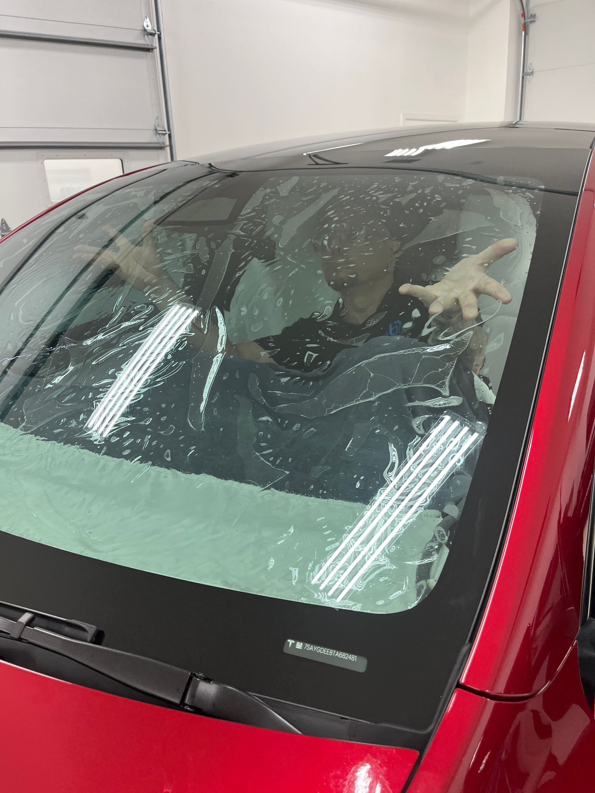 A window tint technician is shown here installing ceramic window tint on the front windshield of a 2026 Tesla Model Y in a clean room at Blue Ocean Auto Spa of Cedar Park Tx