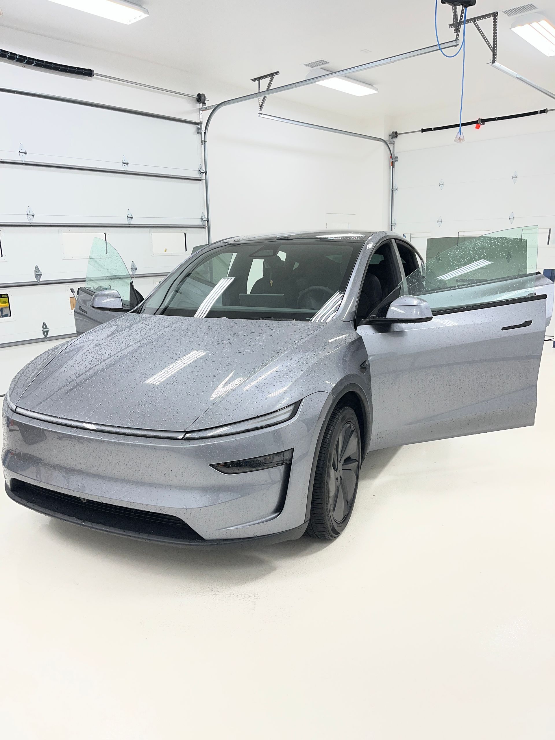 A 2026 Tesla Model Y parked in a clean room with all its doors open to show the front door windows are clear and the second row door windows have factory tint.