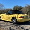 A yellow bmw z3 convertible is parked in a gravel lot