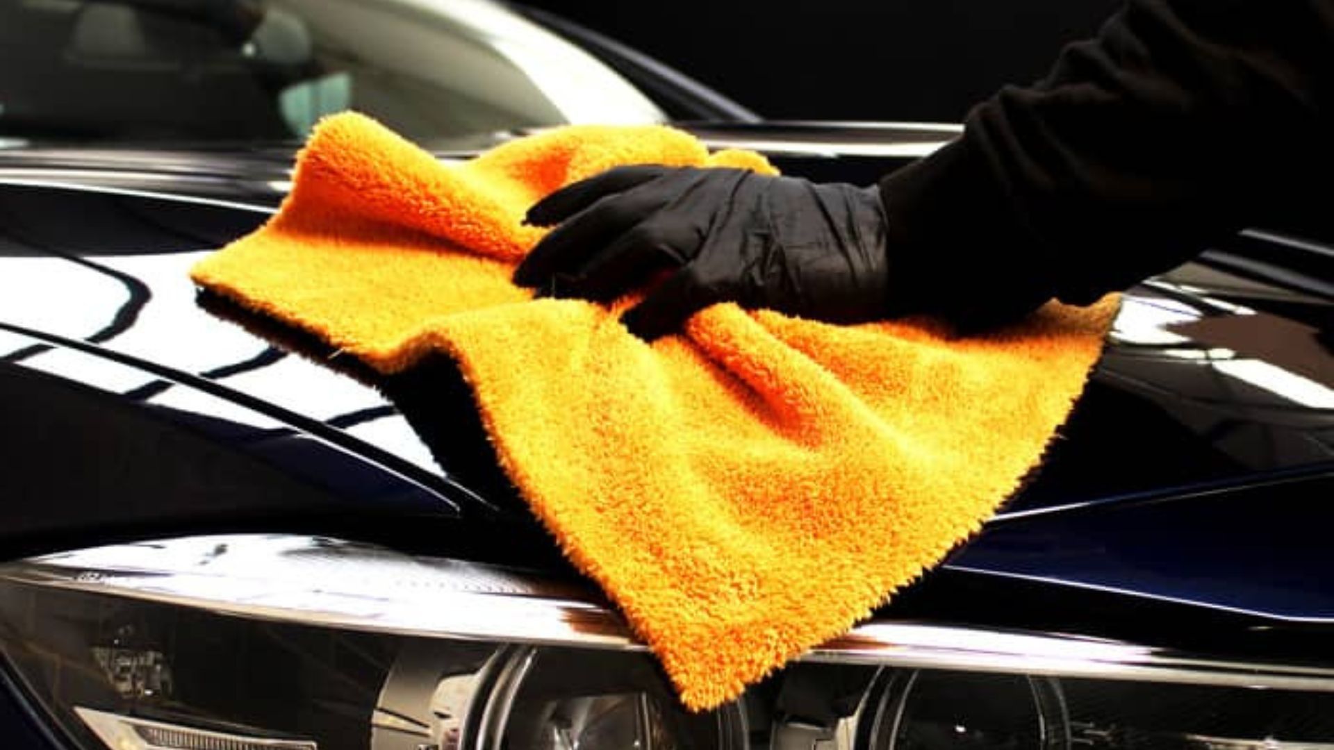 A person buffing ceramic coating onto a car's hood with an orange microfiber cloth to enhance shine 