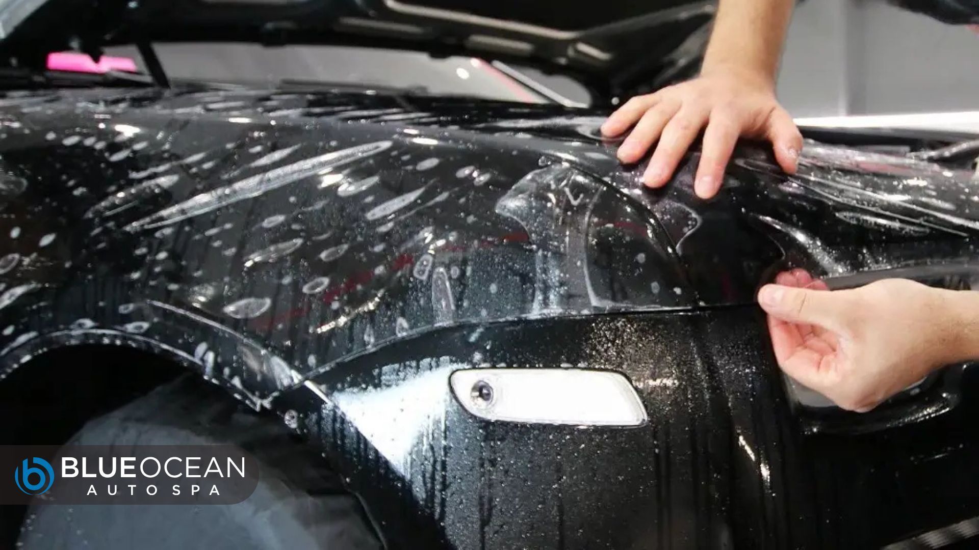 Technician applies paint protection film (PPF) to the fender of a black vehicle