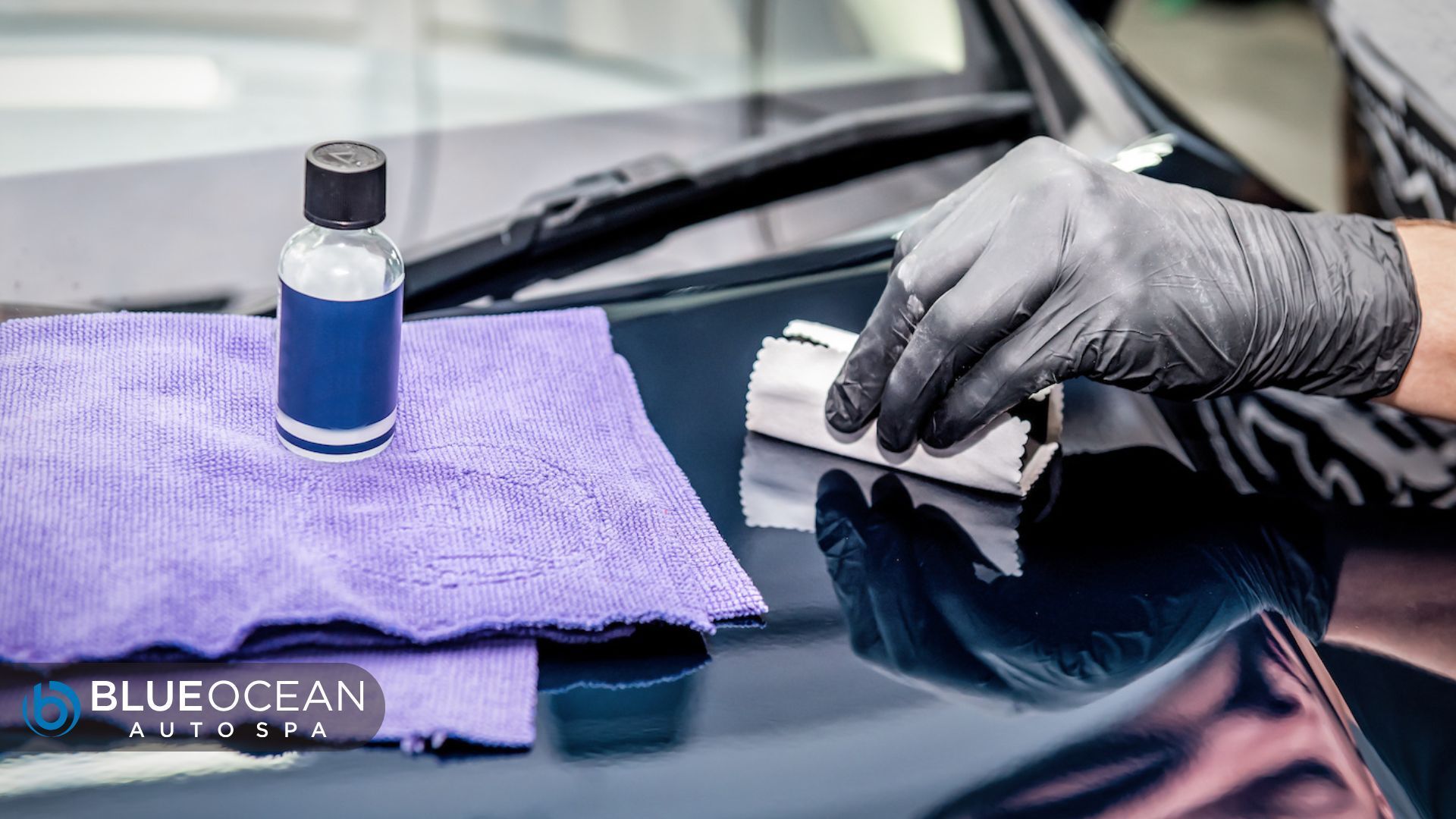 Gloved hand applies ceramic coating to a black car hood using a microfiber cloth, with a coating bot
