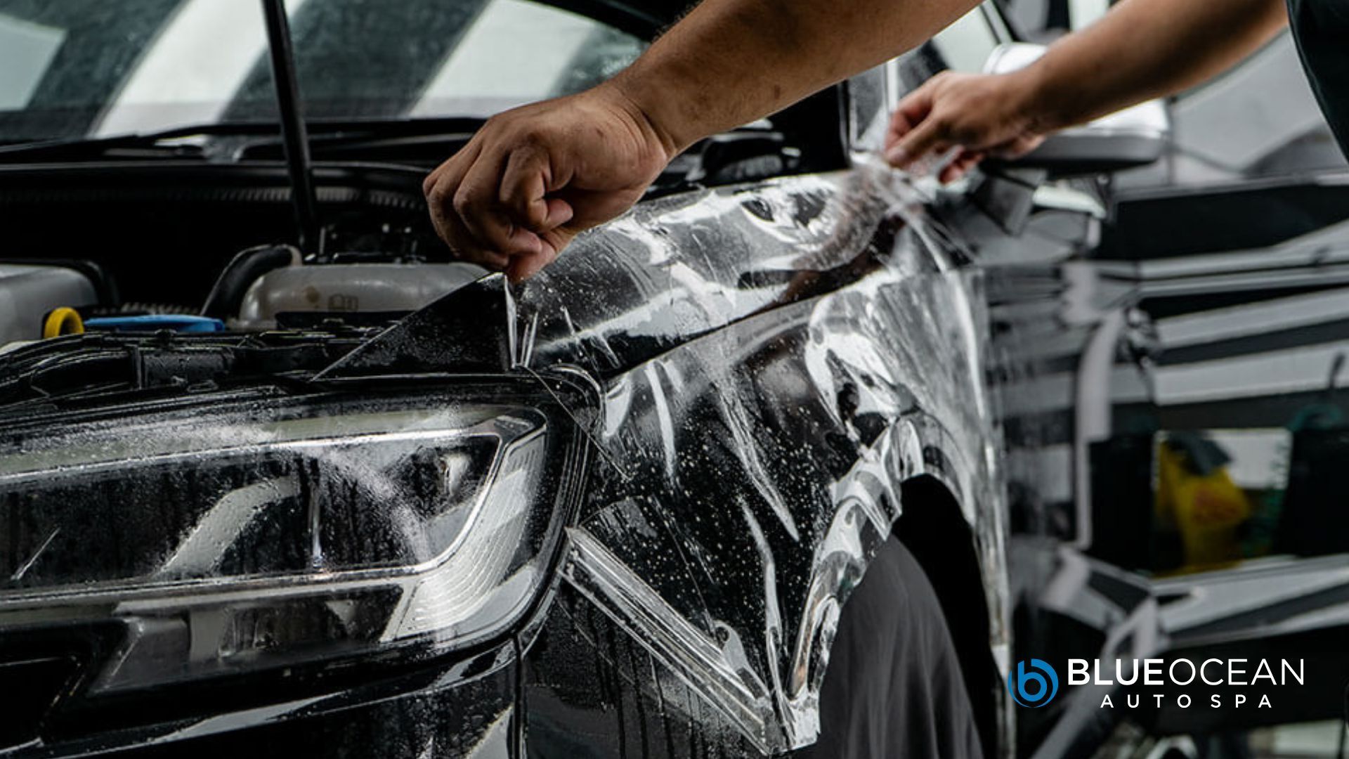 Technician carefully applies clear paint protection film to a black car
