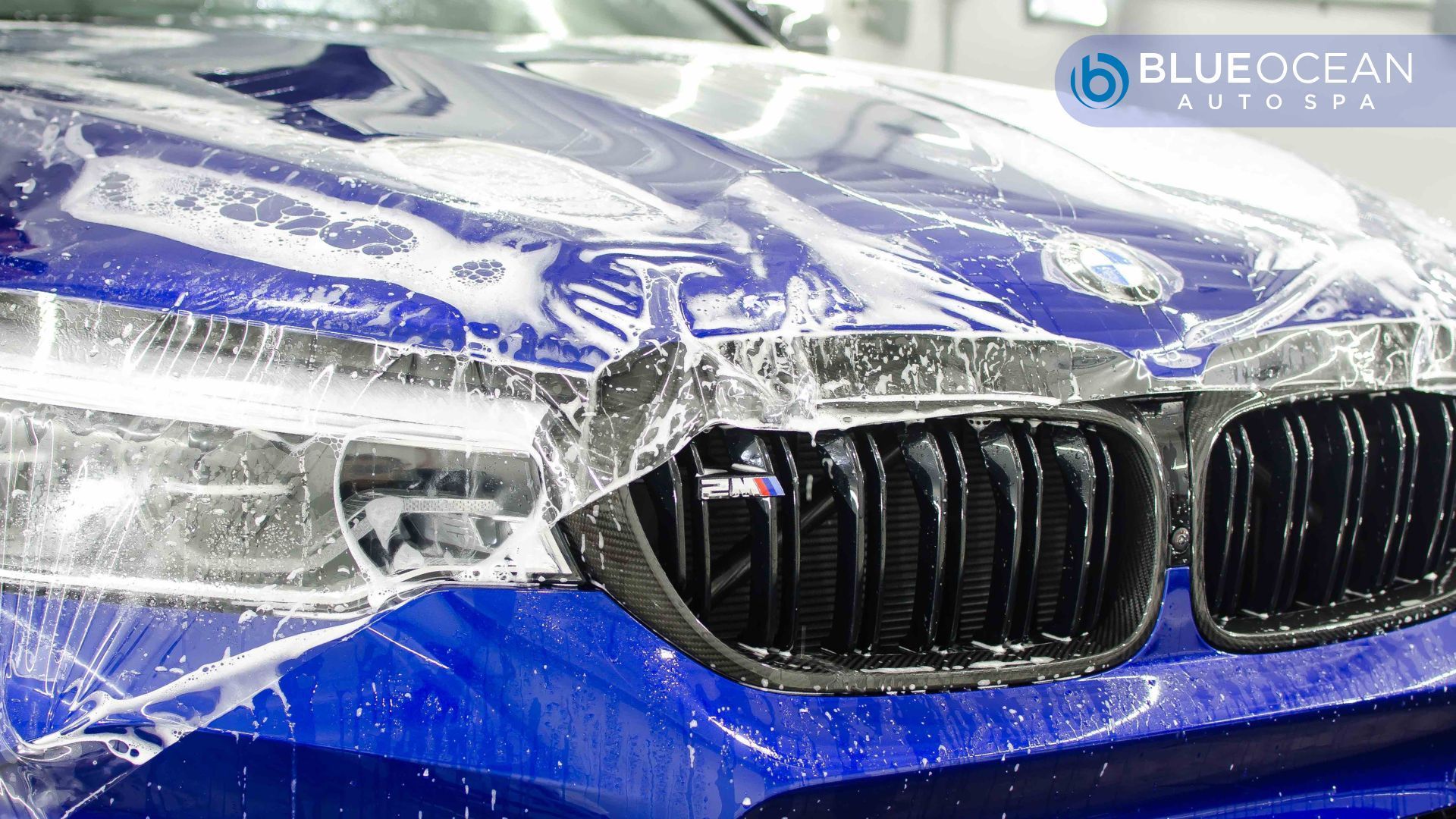 Front of a blue BMW M-series car with a wet, clear paint protection film being applied