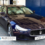 A black maserati ghibli is parked in front of a blue building.