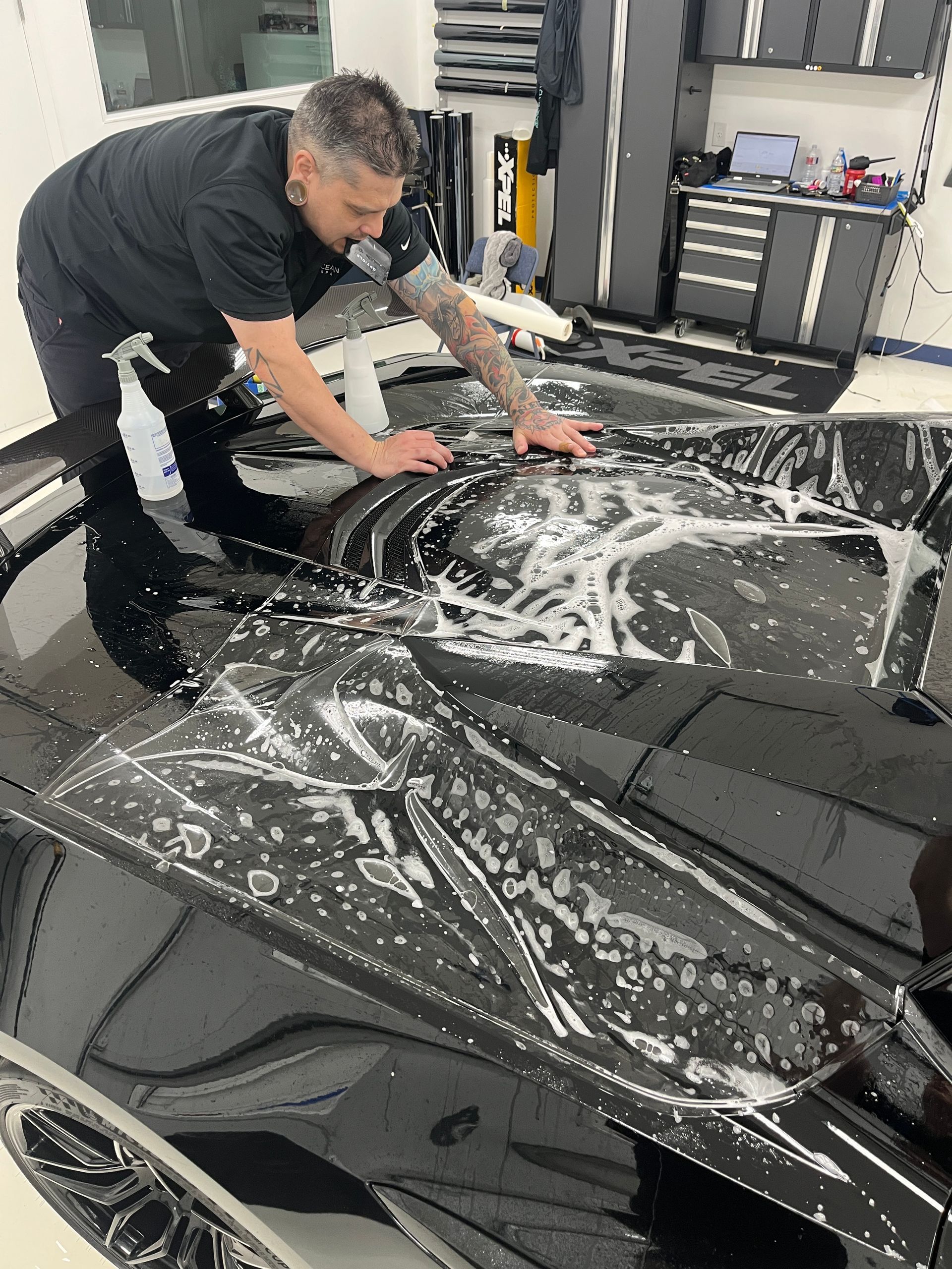 A man is covering the hood of a blue car with plastic wrap.