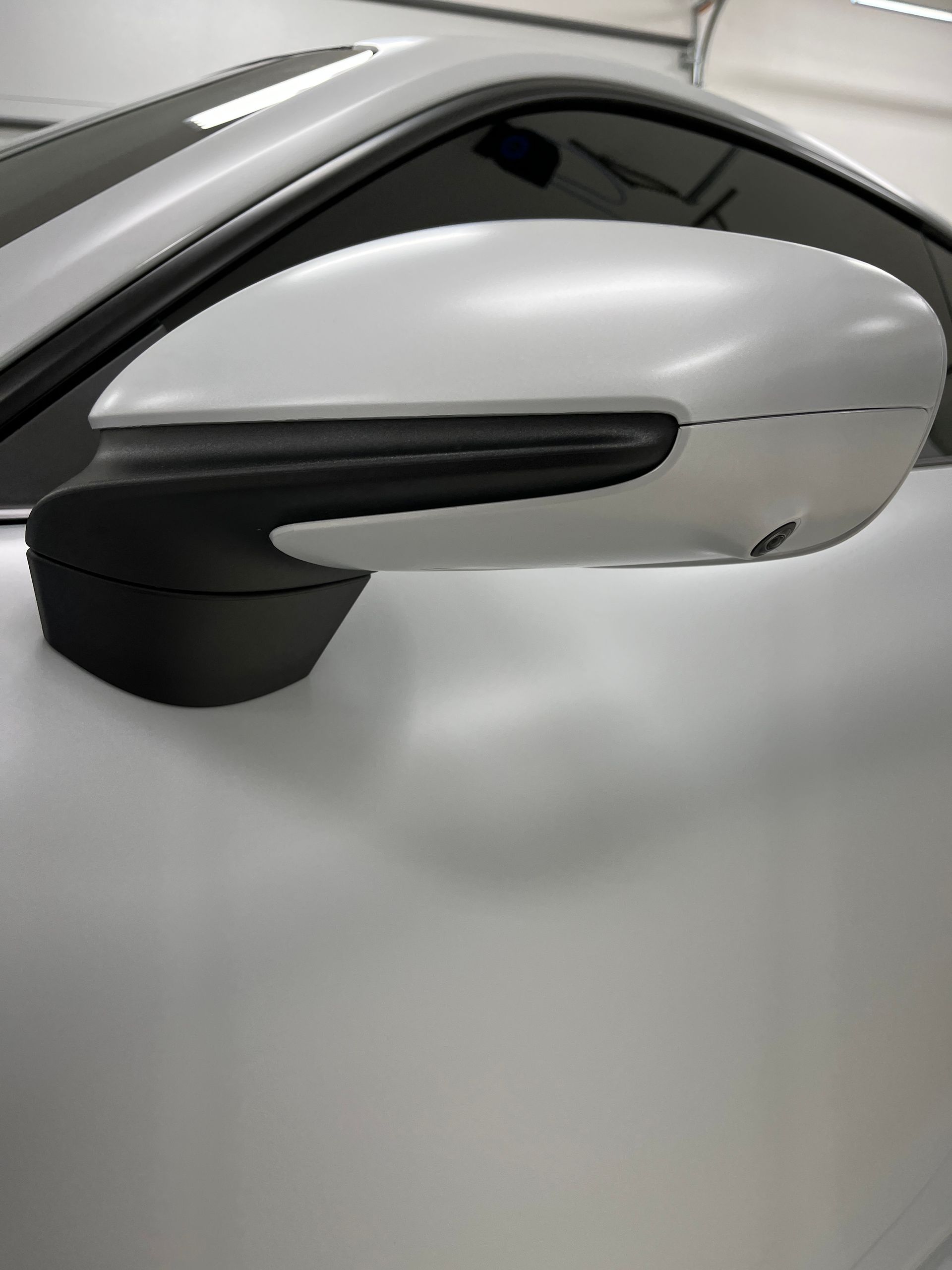Gray car side mirror against a gray car body, with black trim.