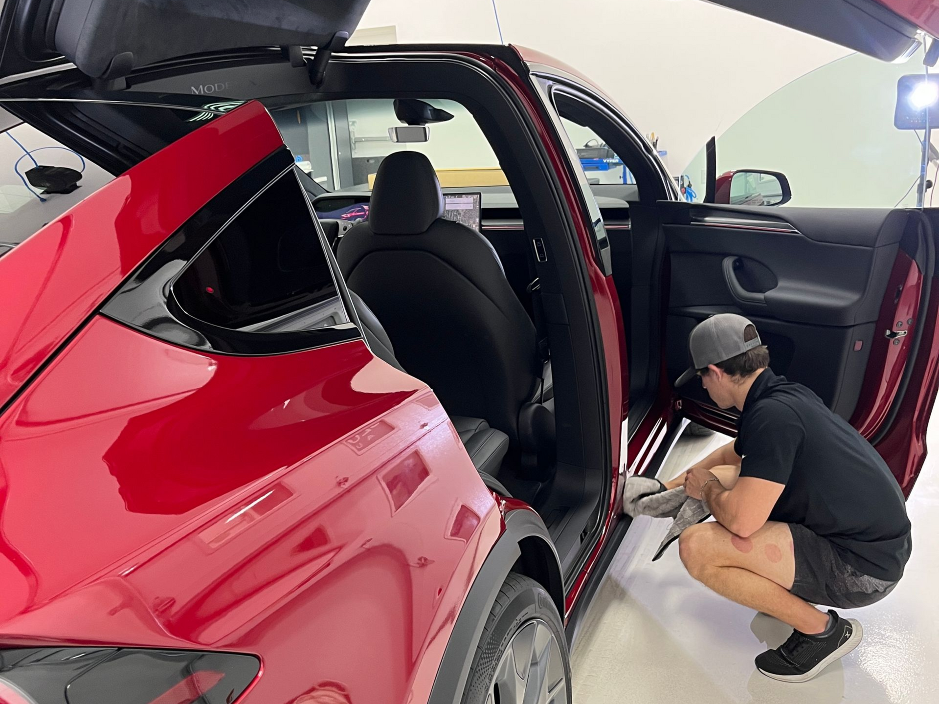 Man cleaning the door frame of a red Tesla, in a garage.