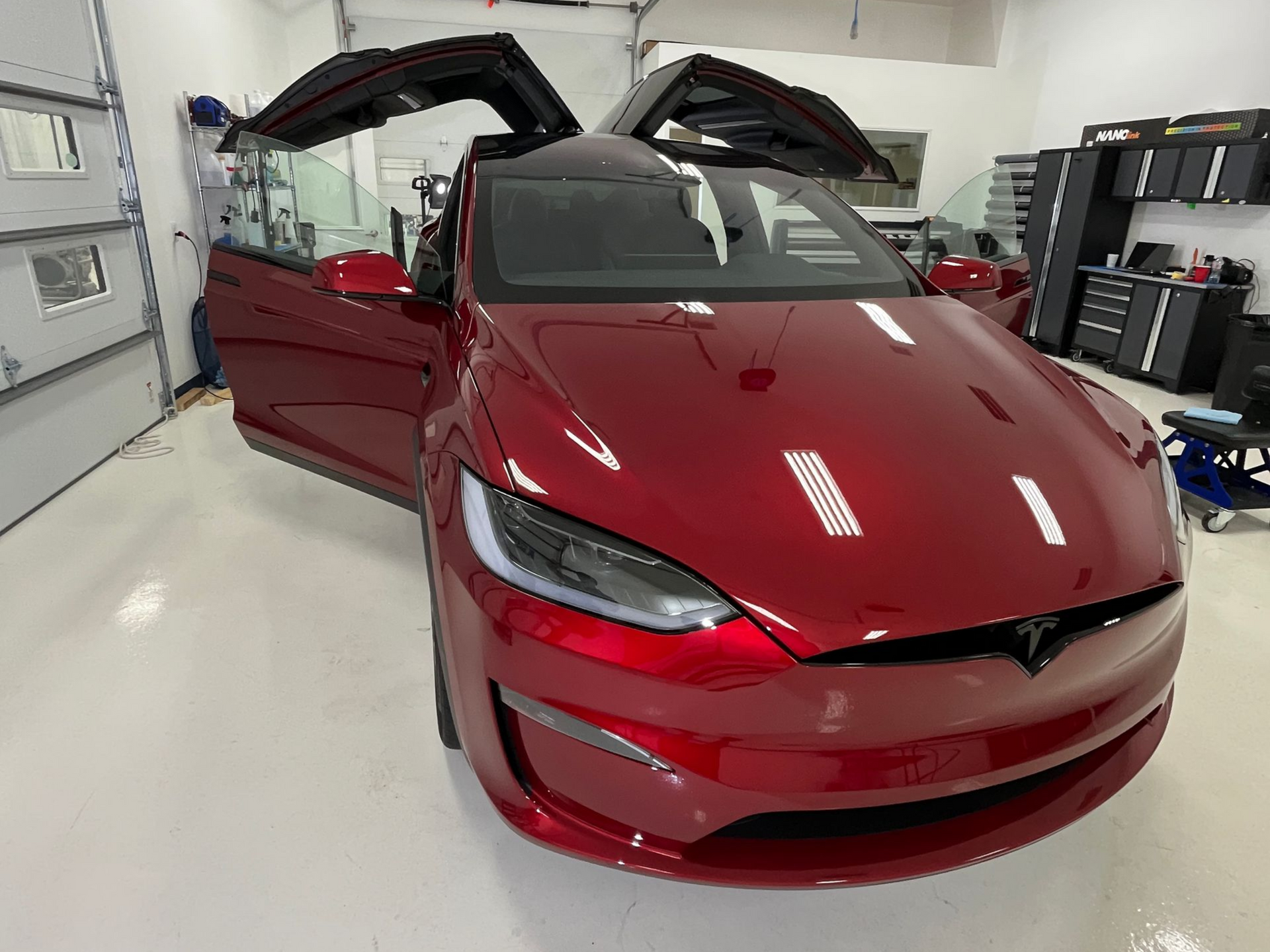 Red Tesla Model X with gullwing doors open in a brightly lit garage.