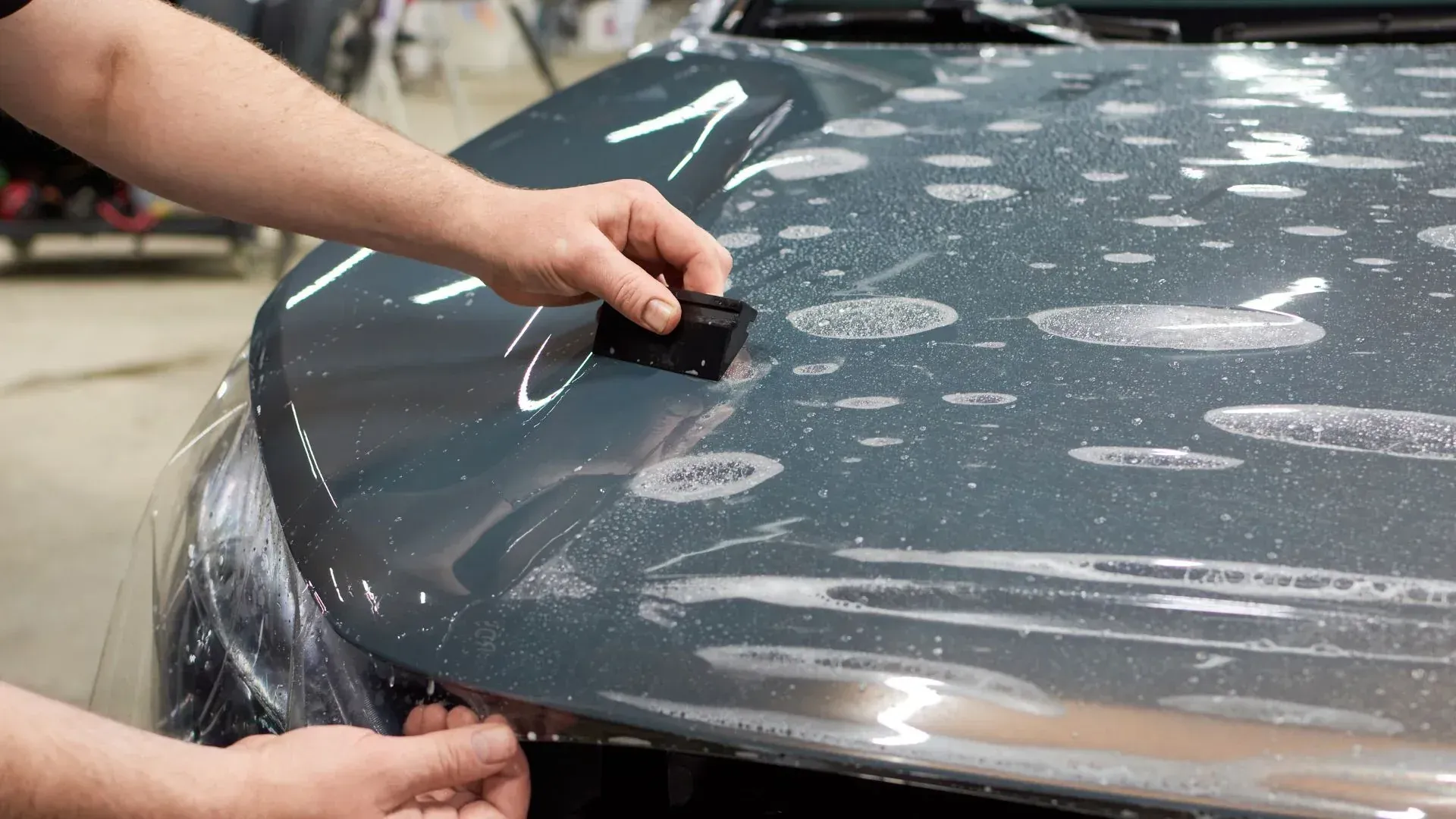 Close-up of a technician applying paint protection film on a car hood using a squeegee to remove air