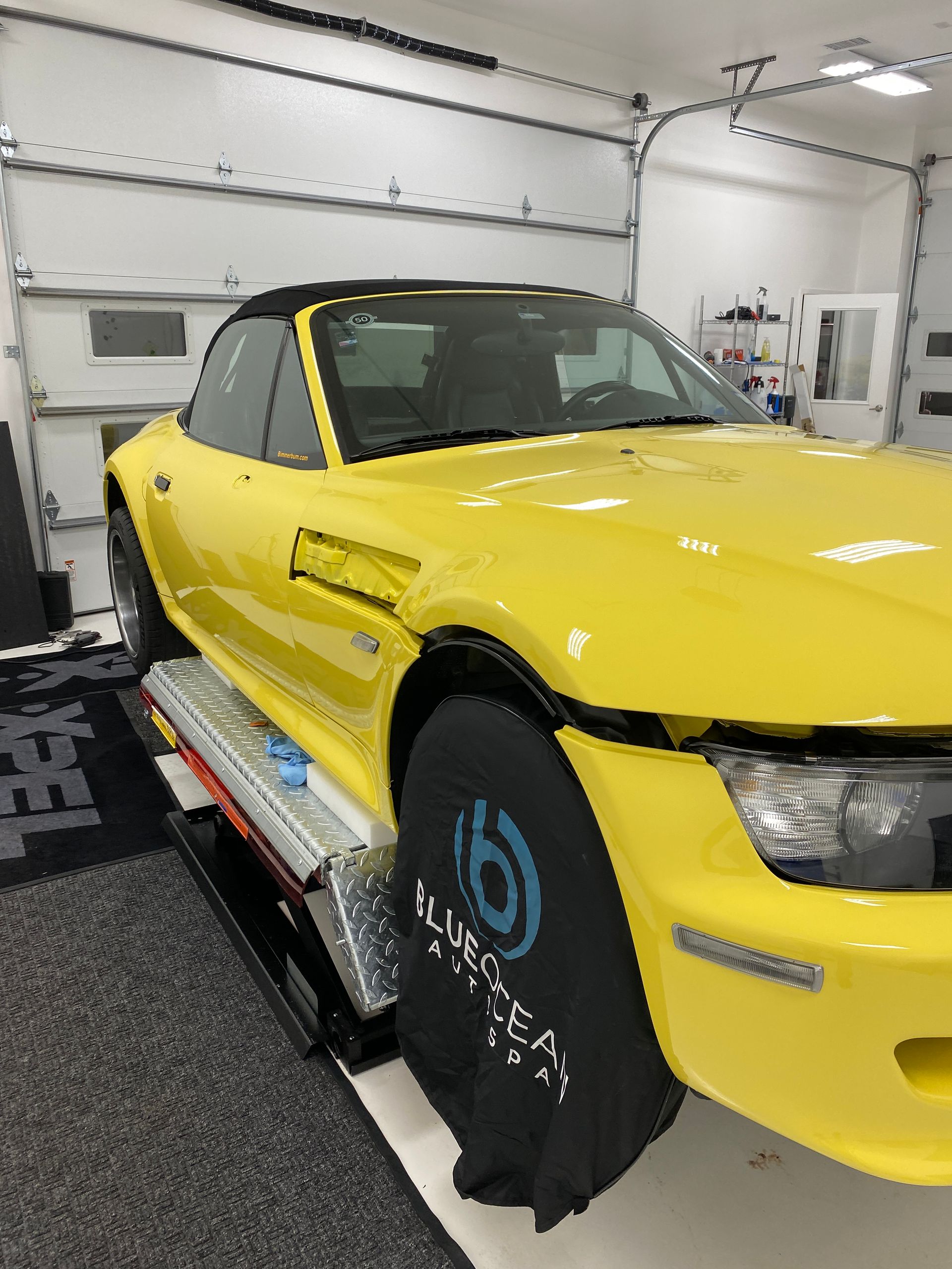 A yellow car is parked in a garage with a black tire cover on it.