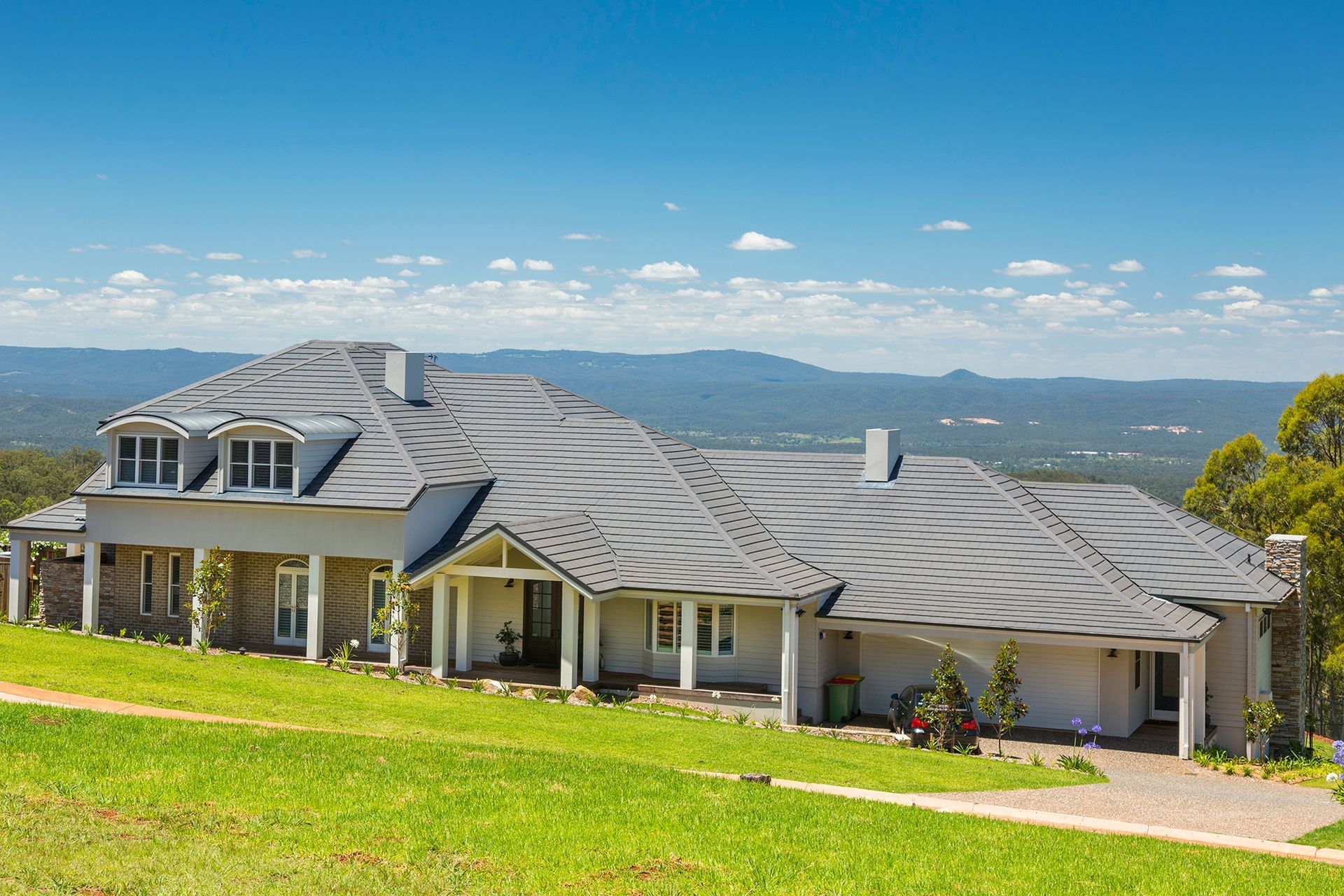 A Large House is Sitting on Top of a Grassy Hill — Mr Roof Tiles in Kingscliff, NSW