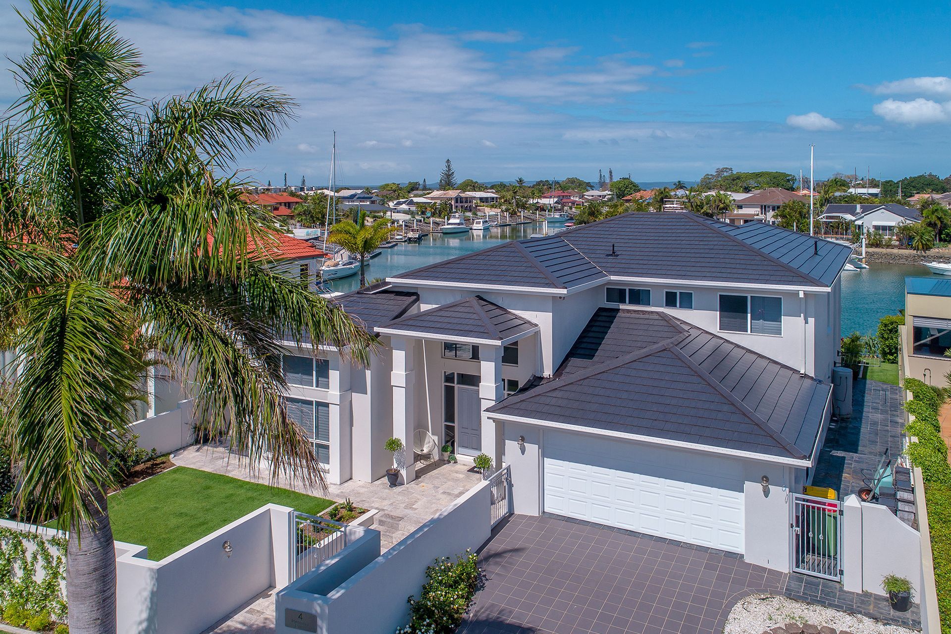 An Aerial View of a Large White House With a Black Roof Surrounded by Palm Trees — Mr. Roof Tiles in Sunshine Coast, QLD
