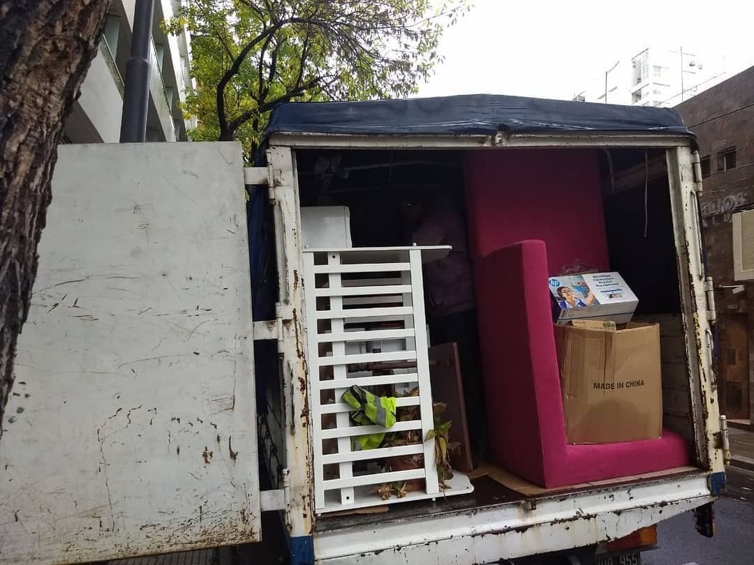 Camión de mudanzas cargado de muebles, entre ellos un sillón rosa, estantes blancos y cajas de cartón.