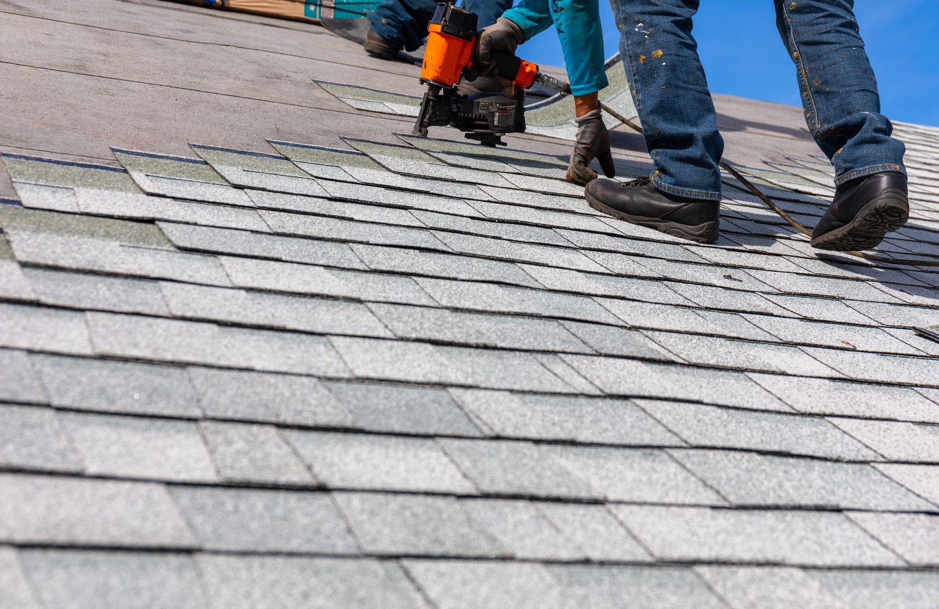 Roofer installing roof shingles with nail gun. Roofer installing roof shingles with nail gun.