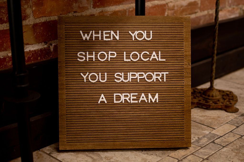 A letter board with the words `` when you shop local you support a dream '' written on it.