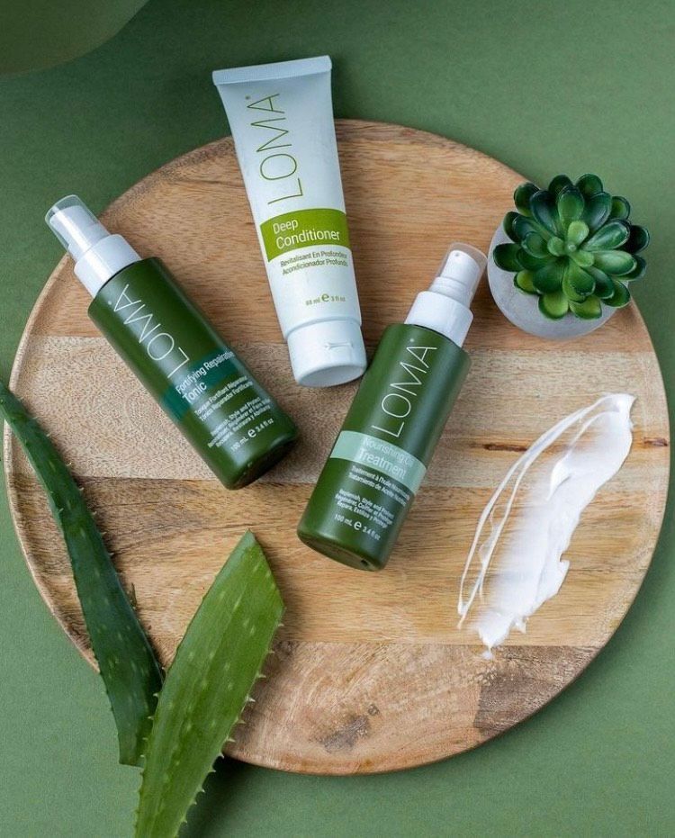 A wooden plate topped with bottles of lotion and aloe vera leaves.