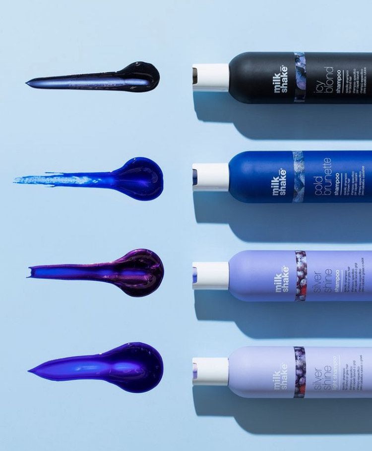 Several bottles of milk shake hair products are lined up on a blue surface.