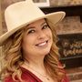 A woman wearing a hat is smiling in front of a sign that says salt kindness