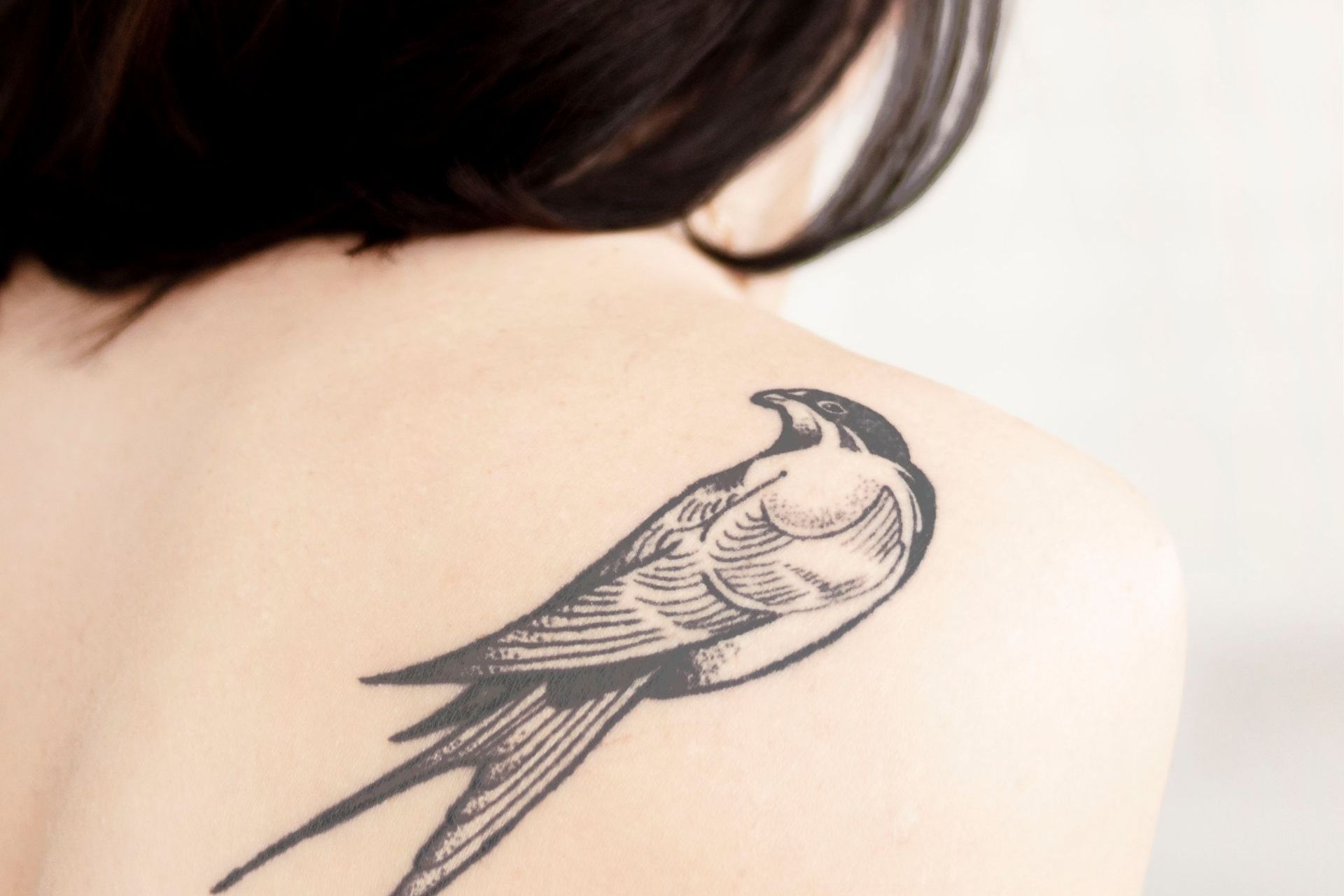 A woman has a tattoo of a bird on her back