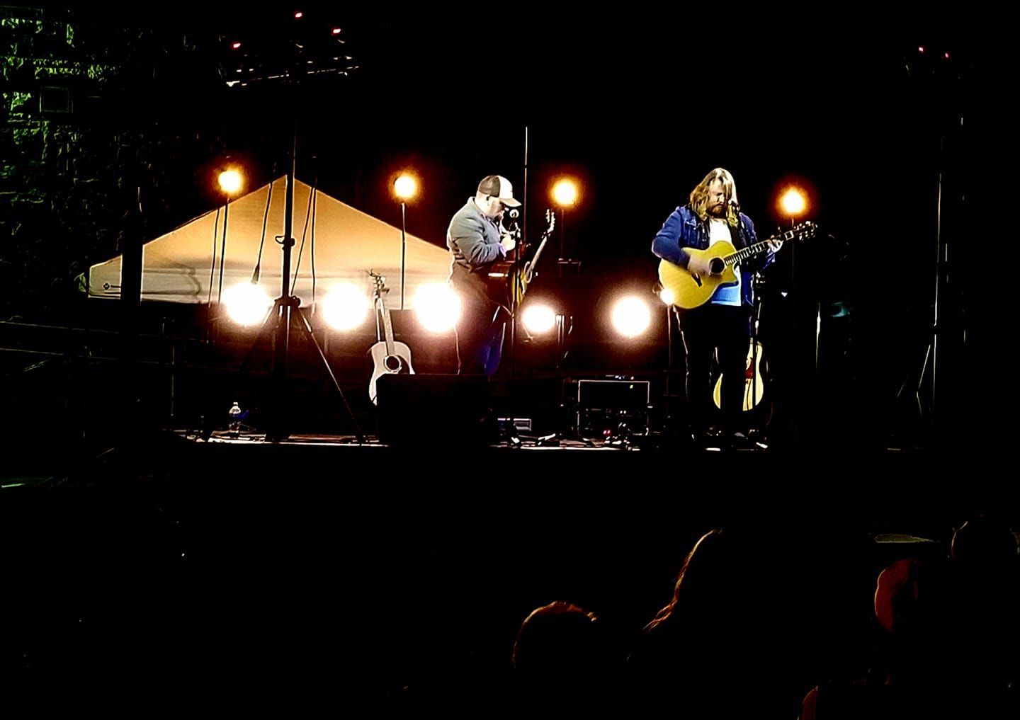 Two men are playing guitars on a stage at night