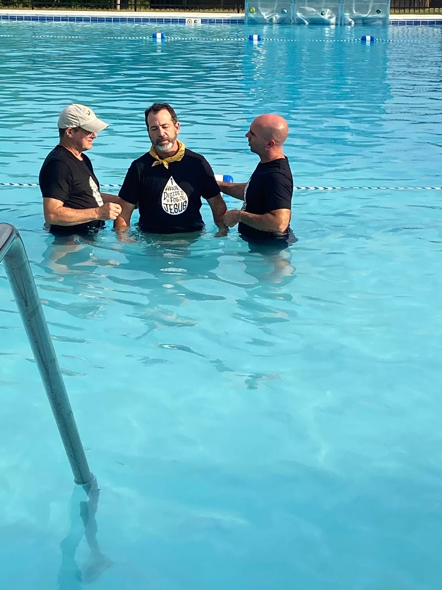 Three men are standing in a swimming pool talking to each other.