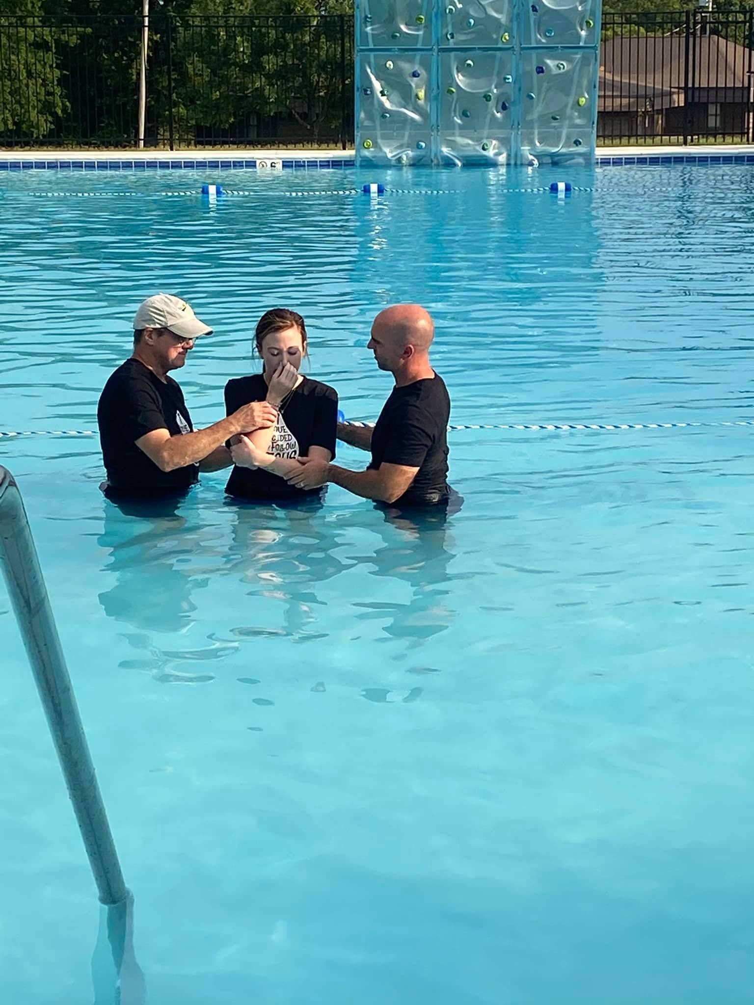 Two men are baptizing a woman in a swimming pool.