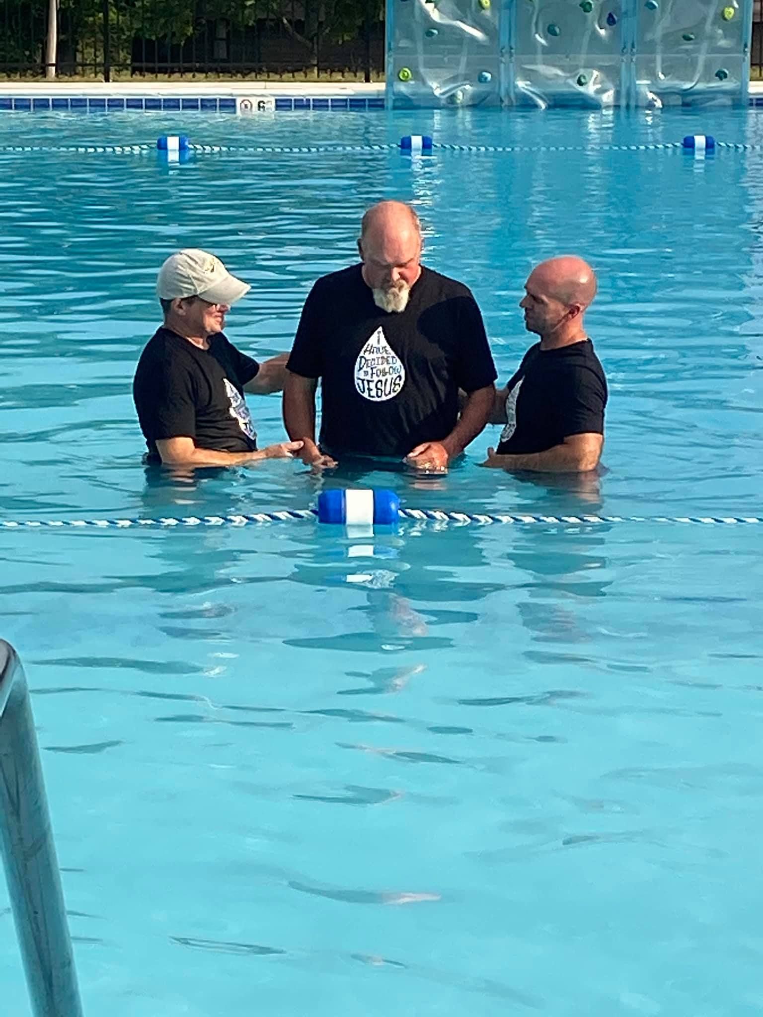Three men are standing in a swimming pool talking to each other.