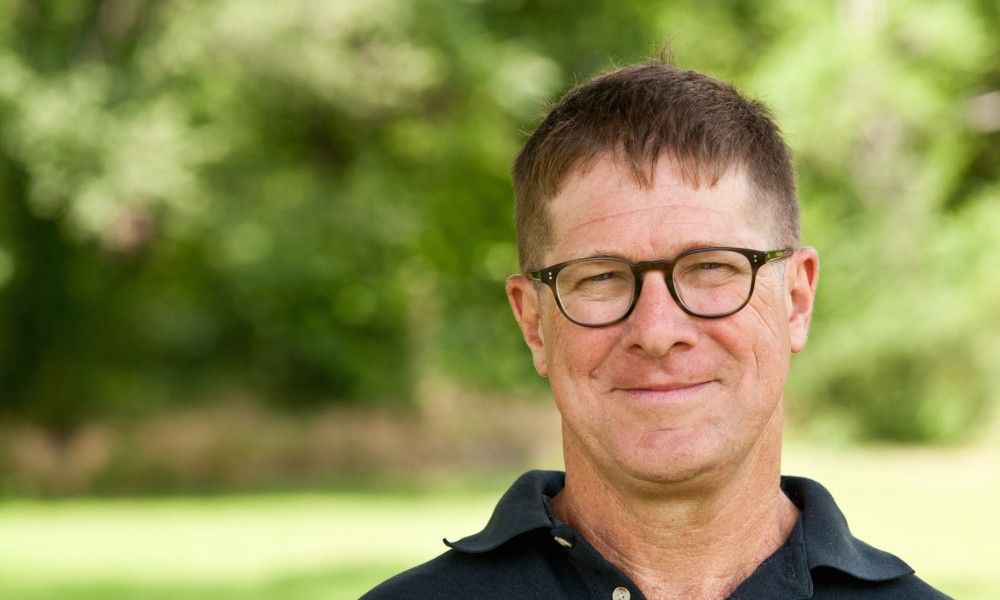 A man wearing glasses and a black shirt is smiling for the camera.
