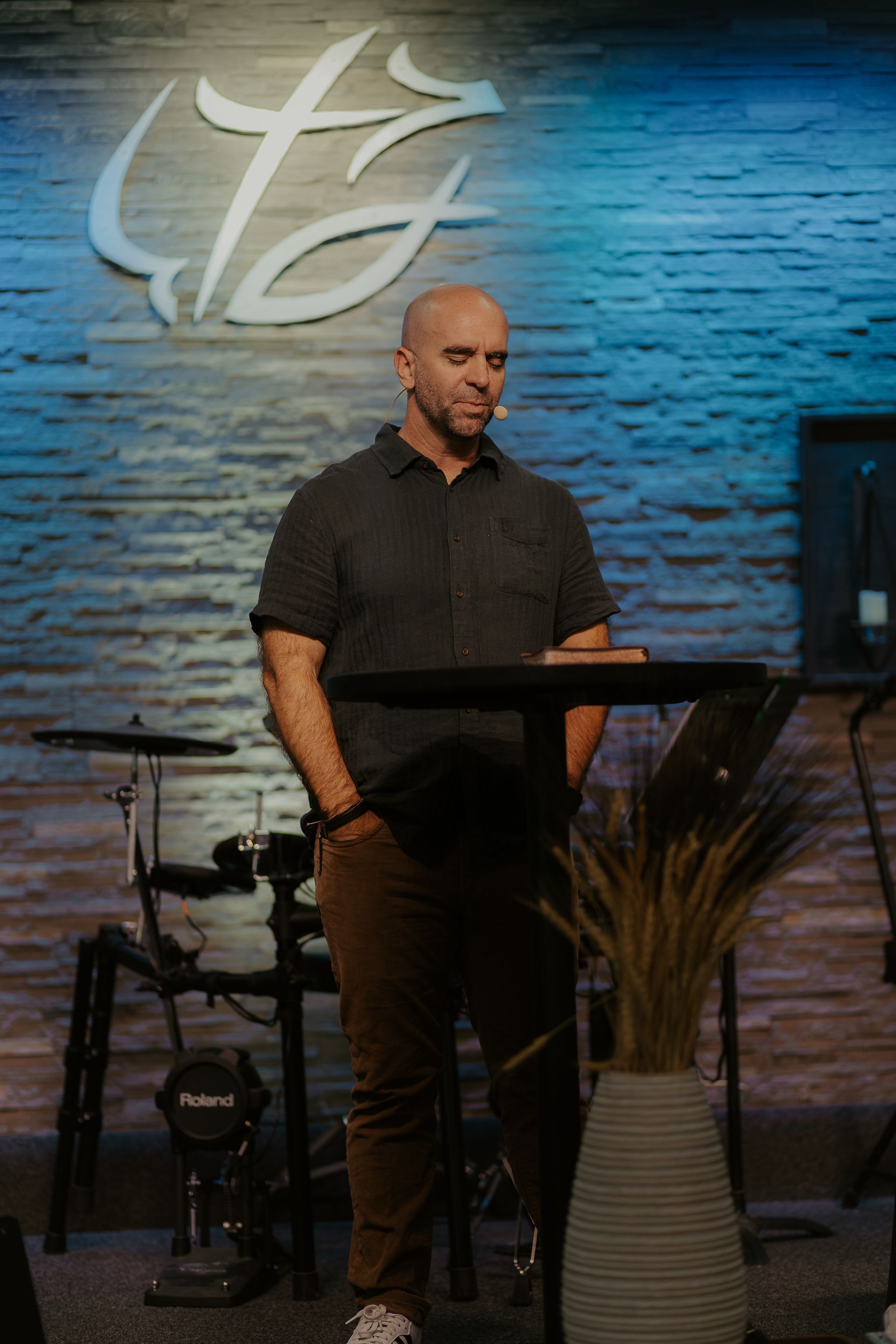 A man is standing at a podium in front of a brick wall.