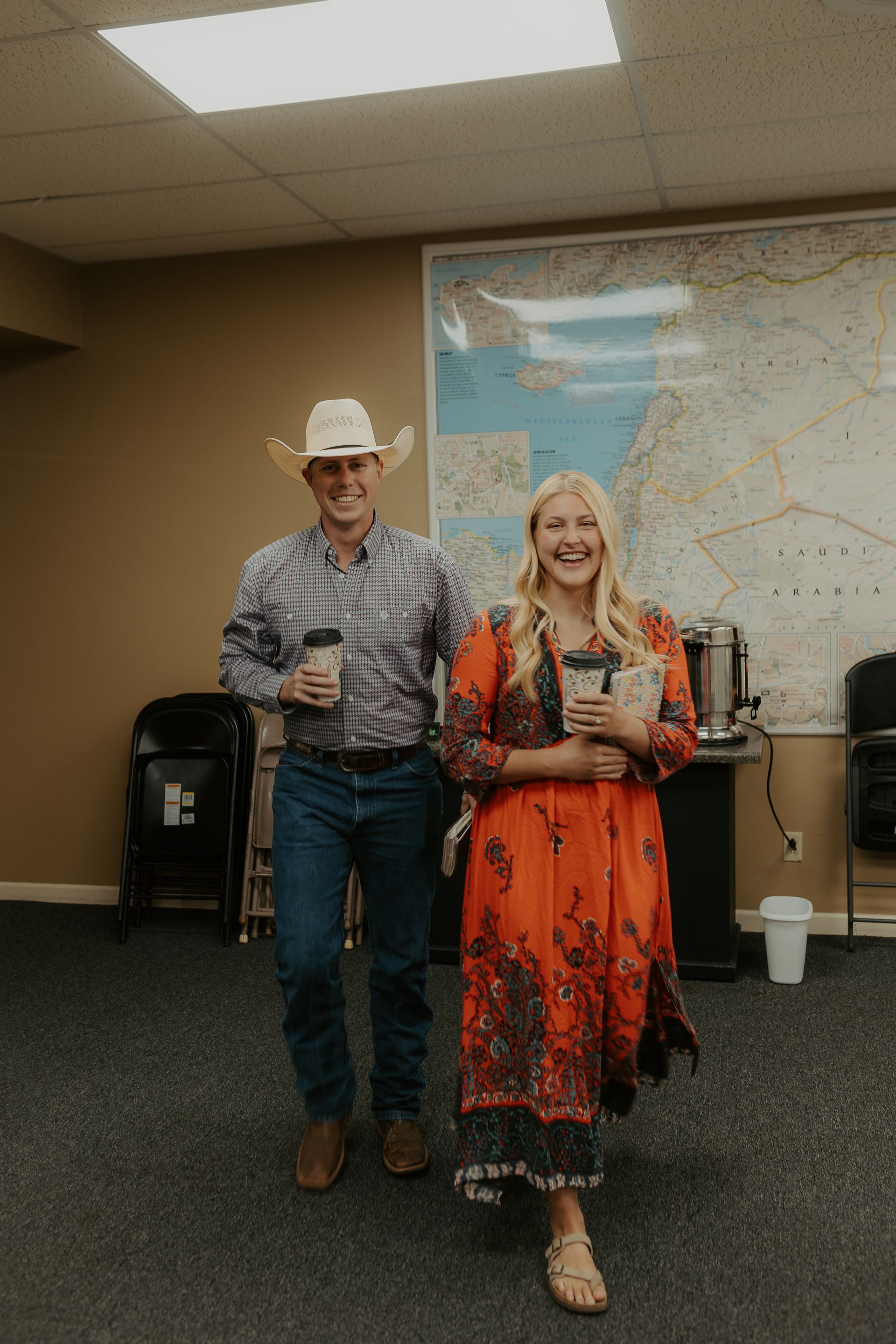 A man and a woman are standing next to each other in a room holding coffee cups.