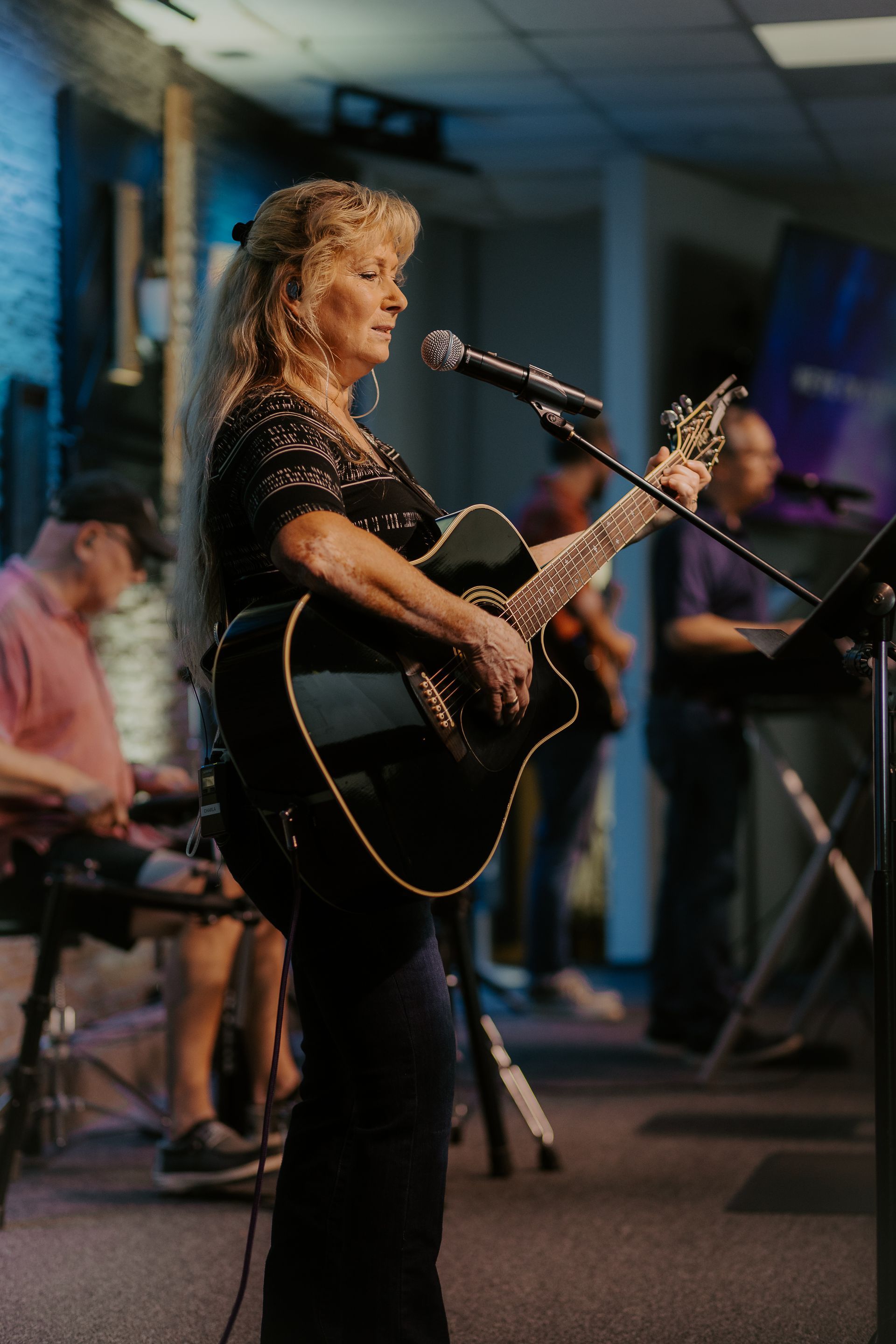 A woman is playing an acoustic guitar and singing into a microphone.