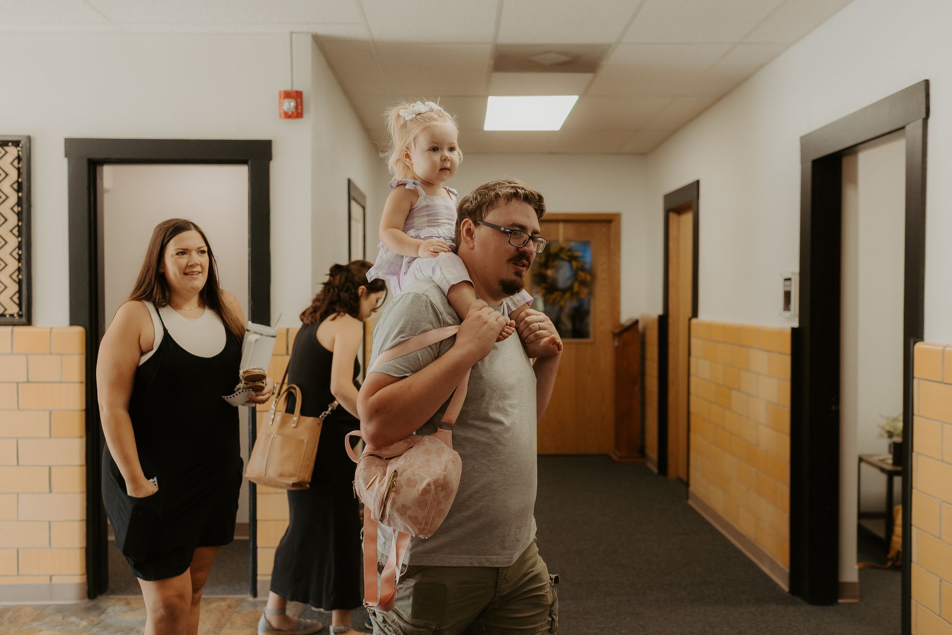 A man is carrying a little girl on his shoulders in a hallway.