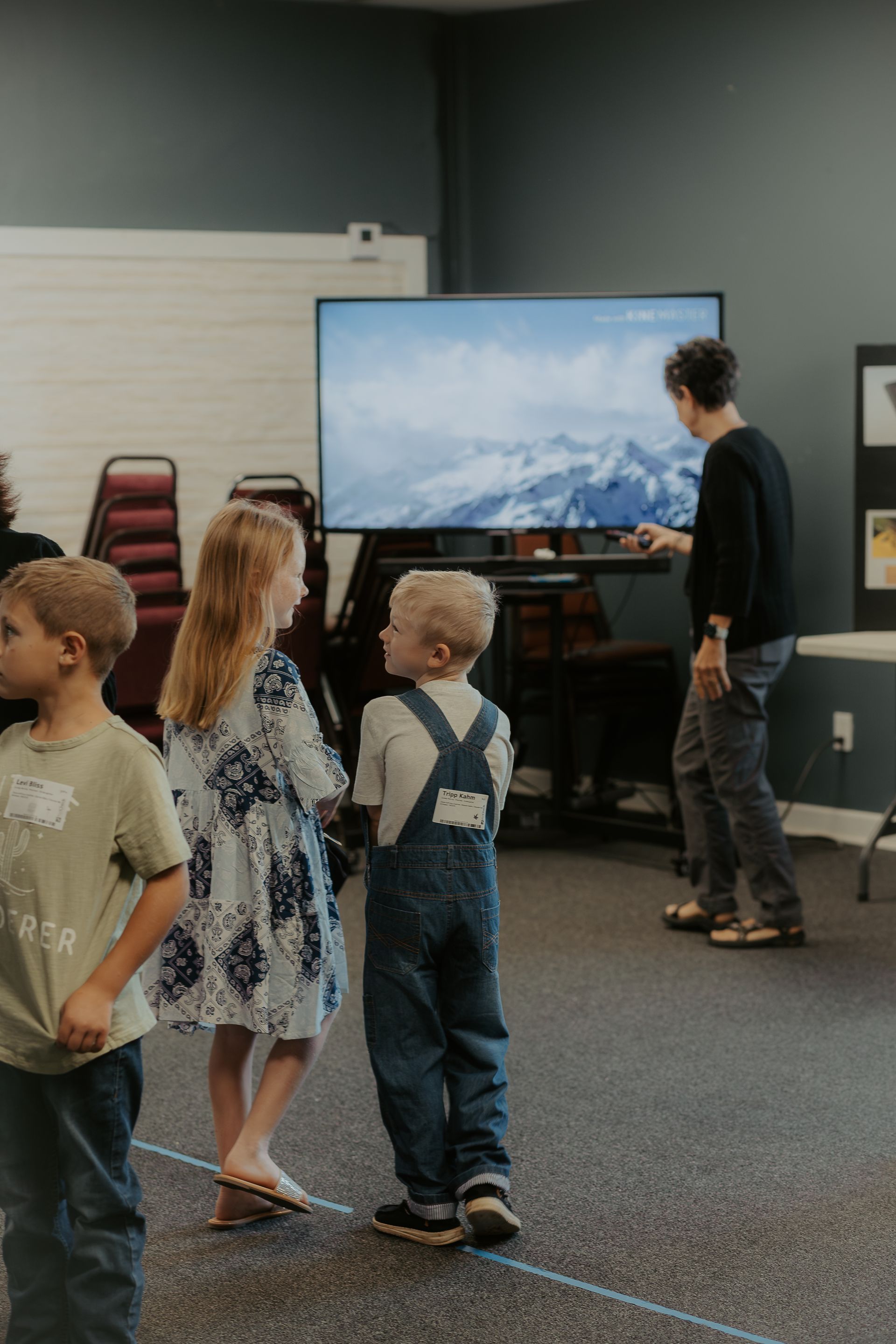 A group of children are standing in a room watching a television.