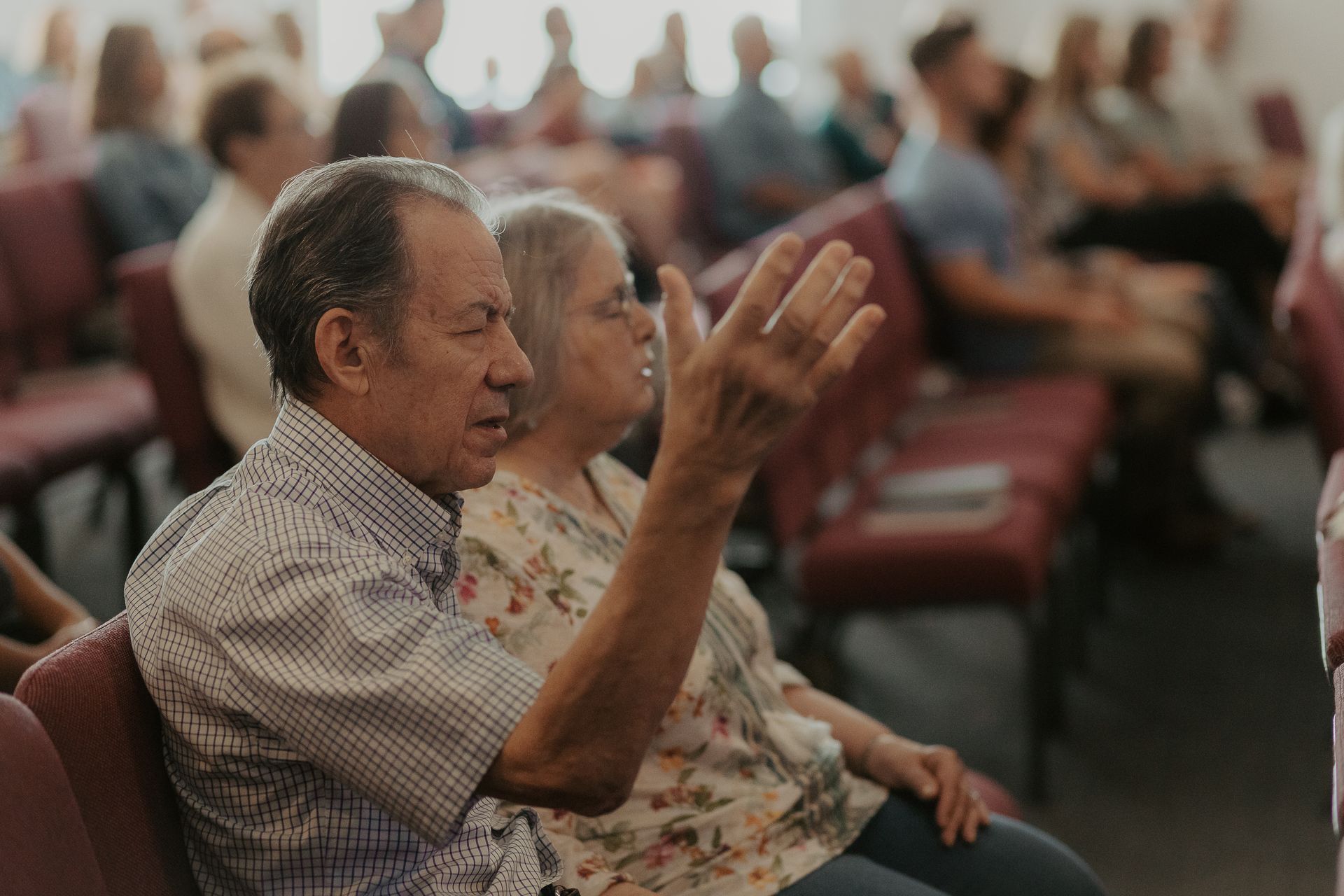 A man and a woman are sitting in a church with their hands in the air.