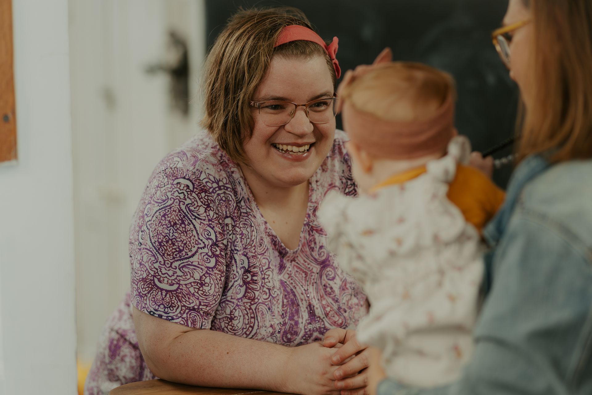 Two women are sitting at a table holding a baby and smiling.